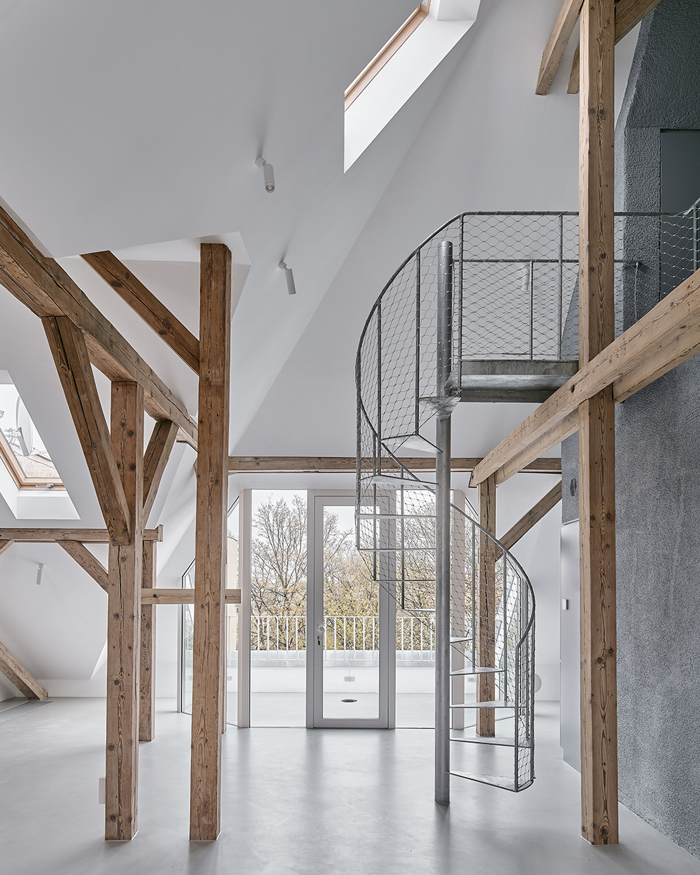 Metal spiral staircase with mesh railings rising through double-height space framed by timber posts and glazed doors