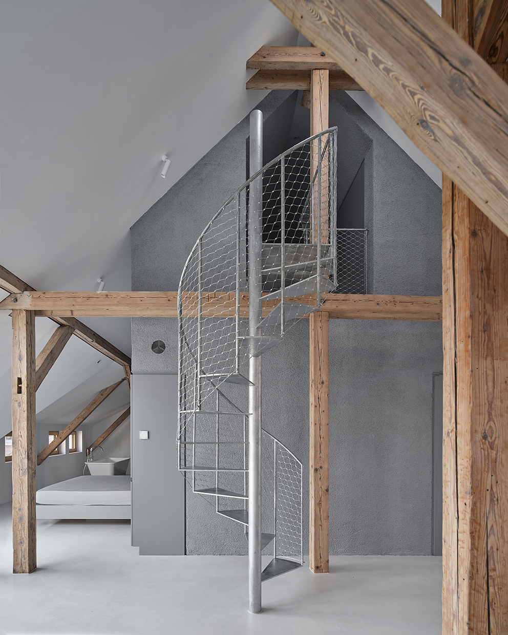 Close-up of wire mesh spiral staircase against charcoal wall plane within timber-framed attic space
