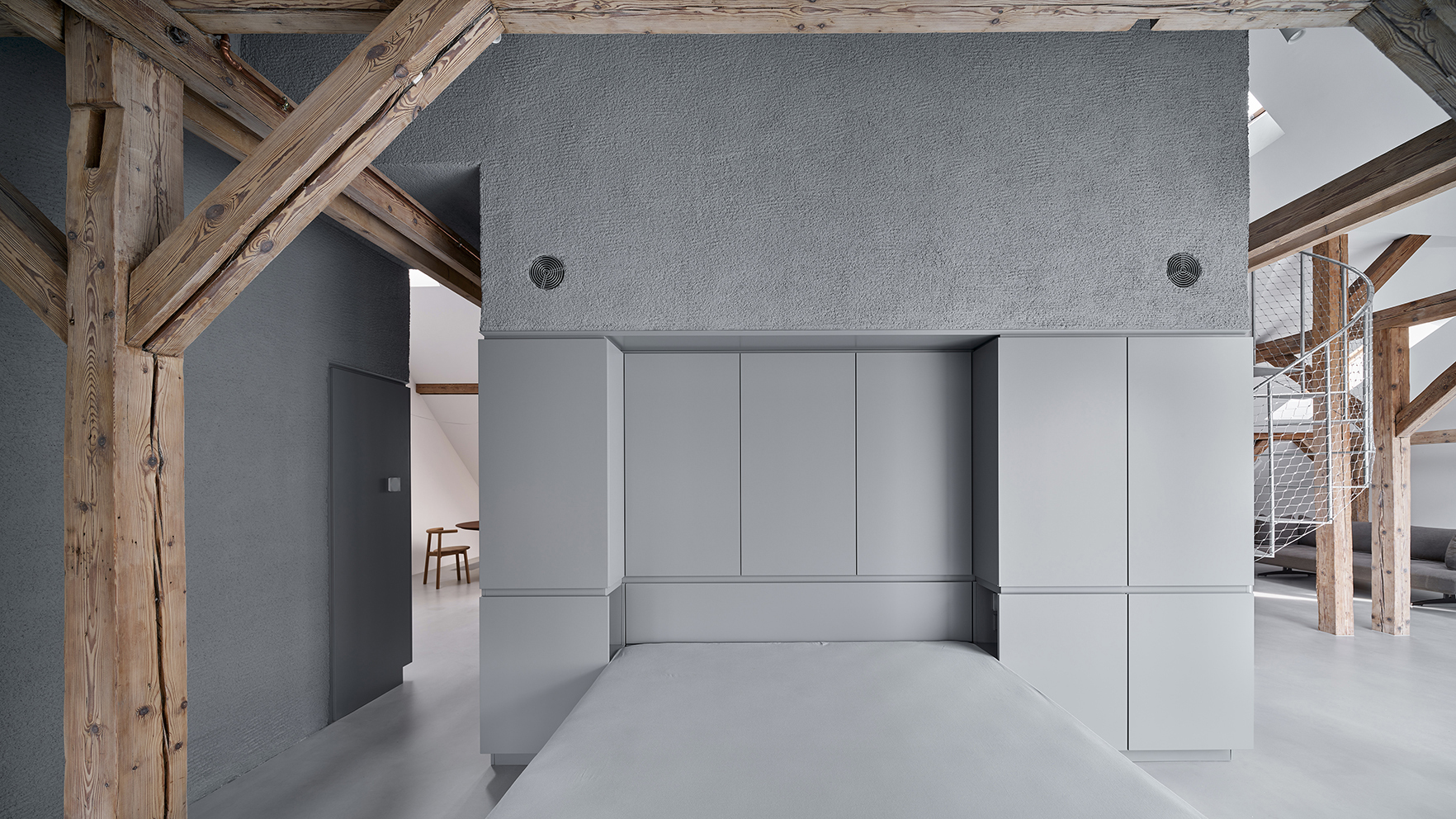 Grey kitchenette volume with flush cabinet panels and concrete countertop surrounded by exposed timber framing