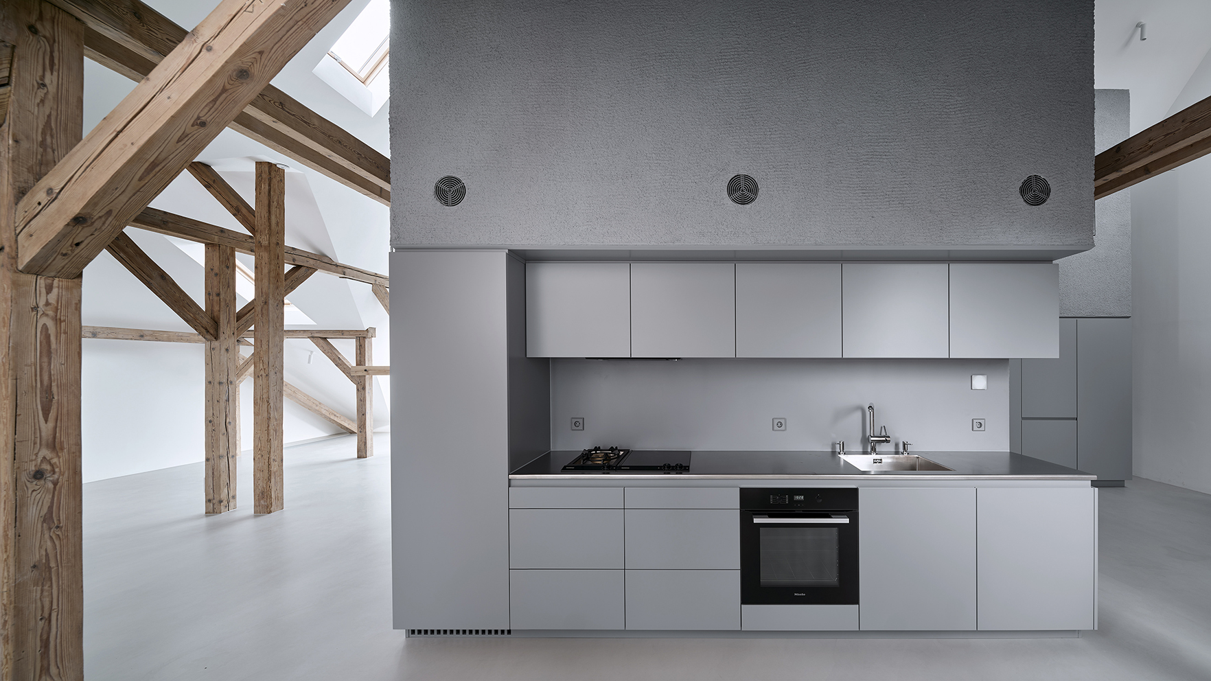 Open kitchen with light grey cabinetry beneath exposed timber roof trusses and skylights