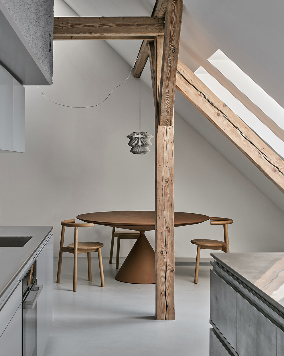 Dining area with pedestal table and chairs beside exposed timber column under sloped ceiling