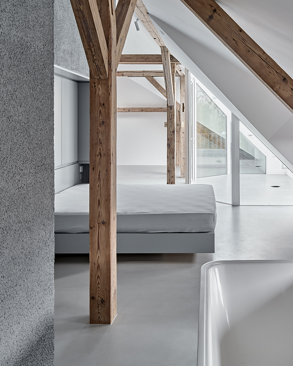 Sleeping area with bed positioned between timber columns beneath sloped ceiling with skylights
