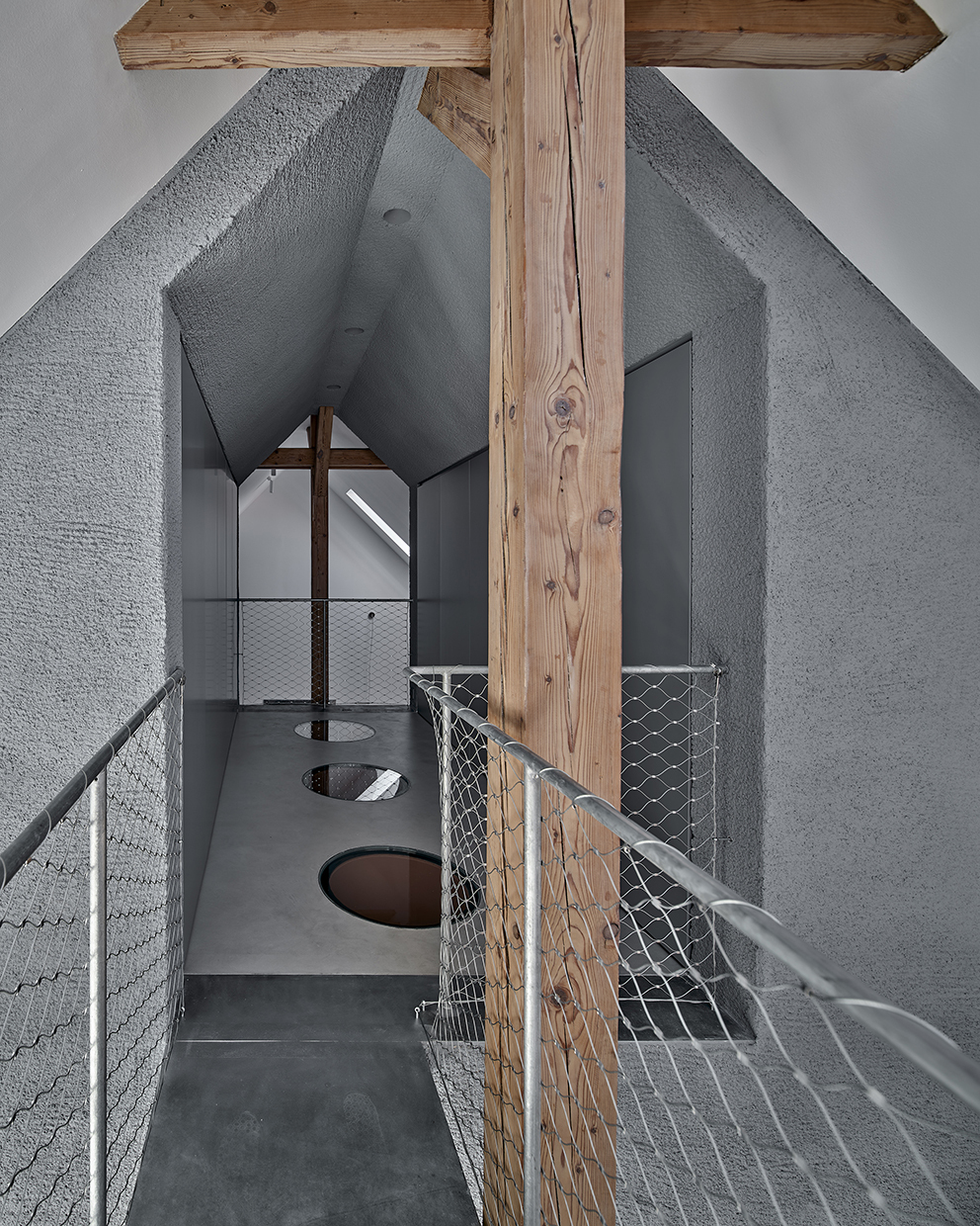 Upper level walkway with wire mesh railing and circular floor openings beside timber post
