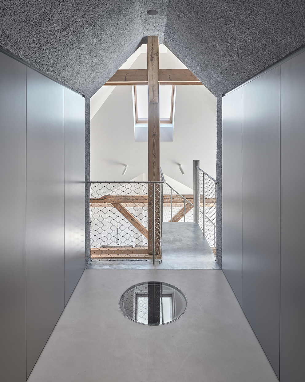 Attic corridor with circular skylight in the polished floor and exposed timber beams under textured ceiling