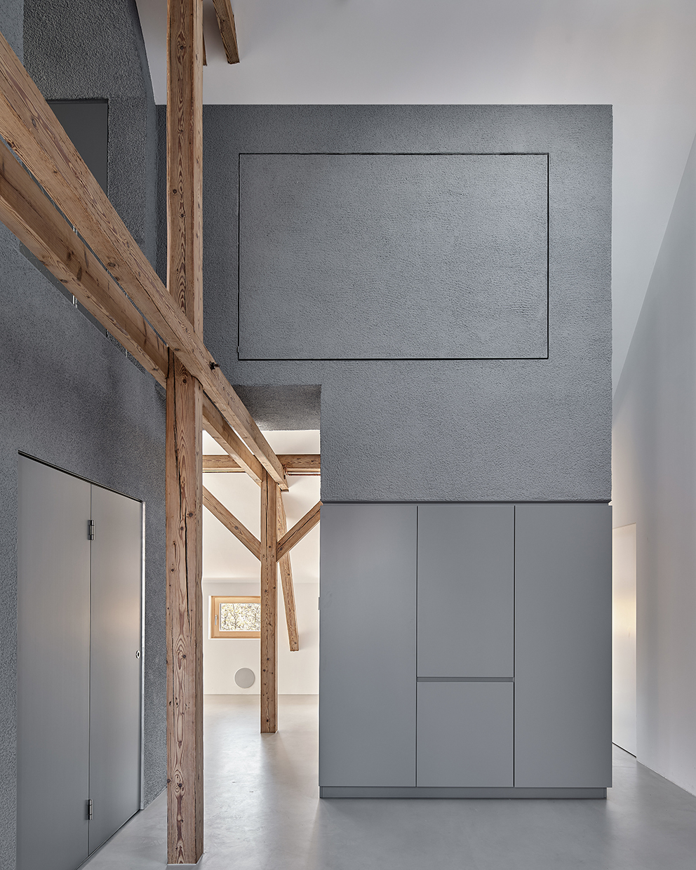 Double-height hallway with exposed timber columns and grey storage wall beneath integrated ceiling panel