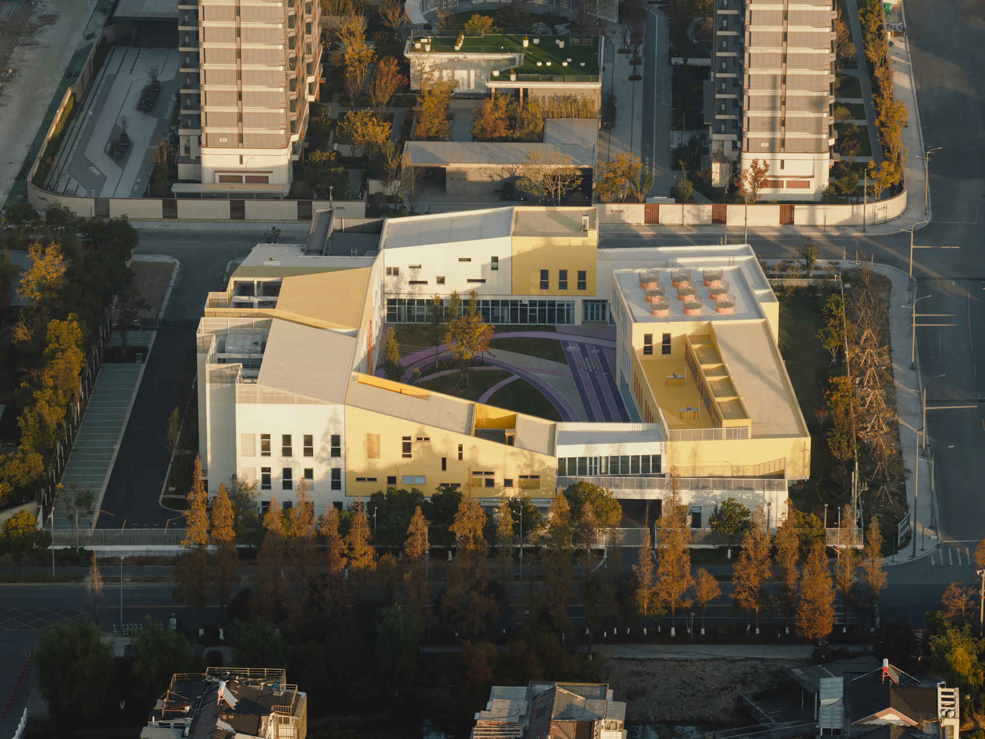 Aerial view of the courtyard enclosure with purple curved pathways surrounded by trees in autumn light