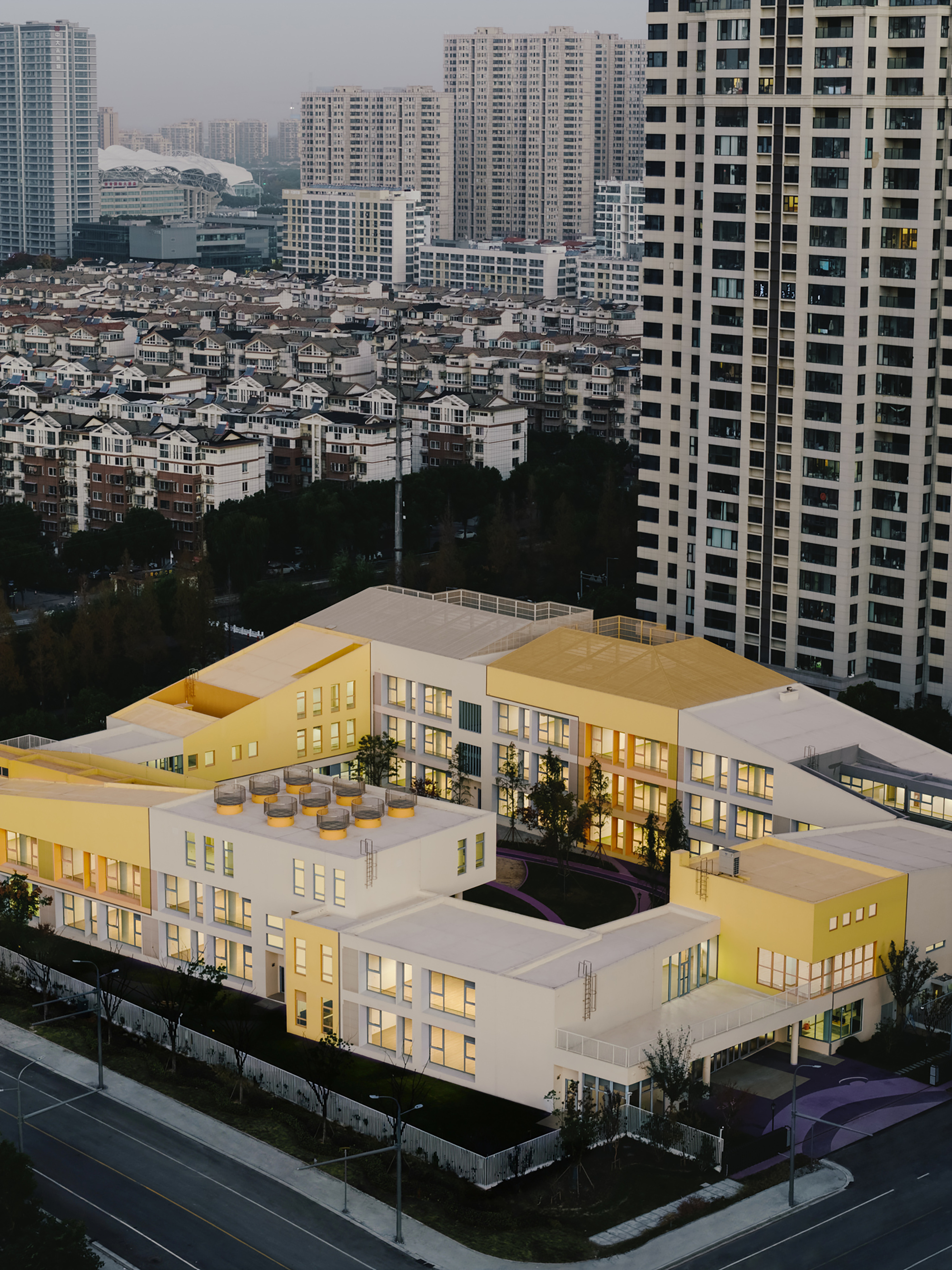 Aerial view of the white terraced school building with interior courtyard surrounded by high-rise towers at dusk