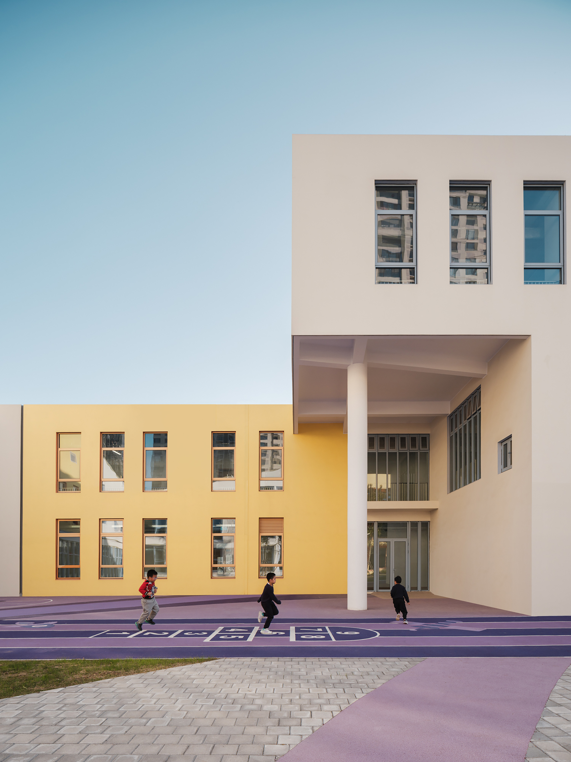 Courtyard view showing yellow and beige facades with a covered entry and children playing on purple pavement