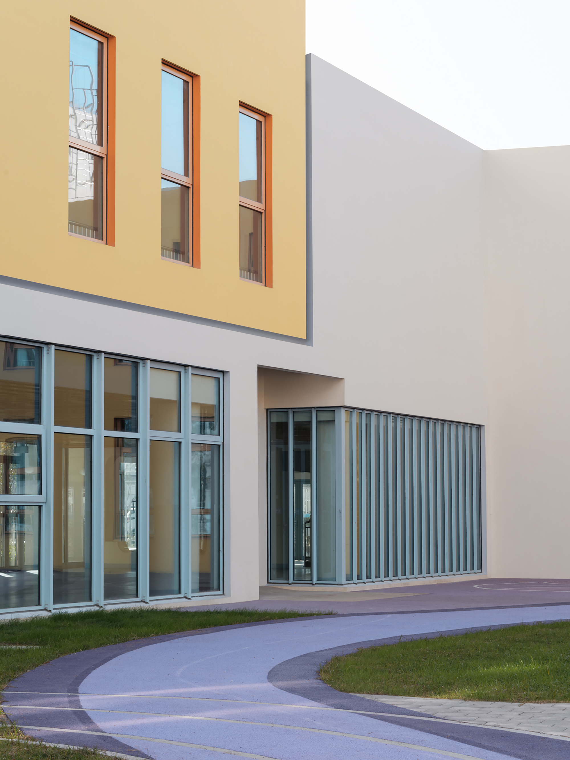 Ground-level view of the entry with glass curtain wall and vertical metal louvres beside a curved pathway