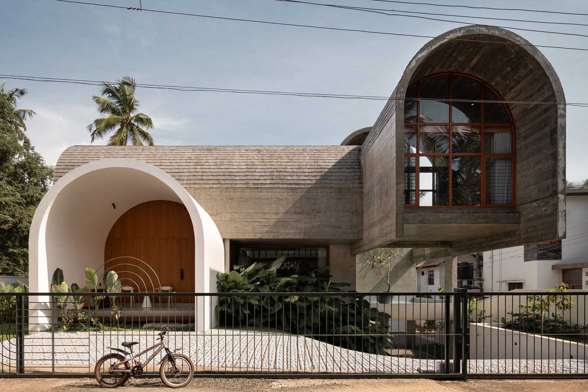 Street view of the concrete facade with arched openings and a bicycle leaning against the metal fence