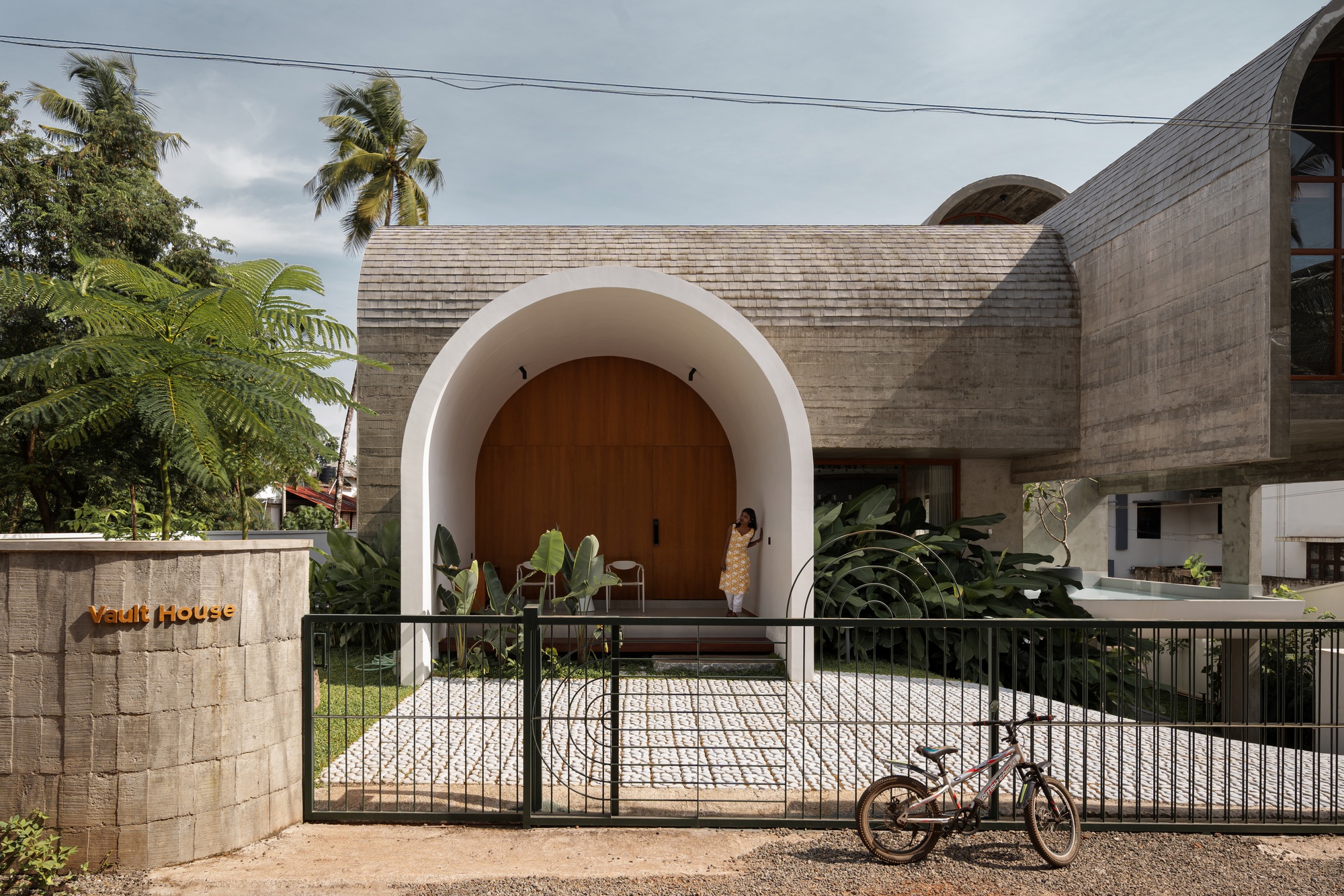 Arched entry portal with timber door and white stucco surround framed by a black metal gate