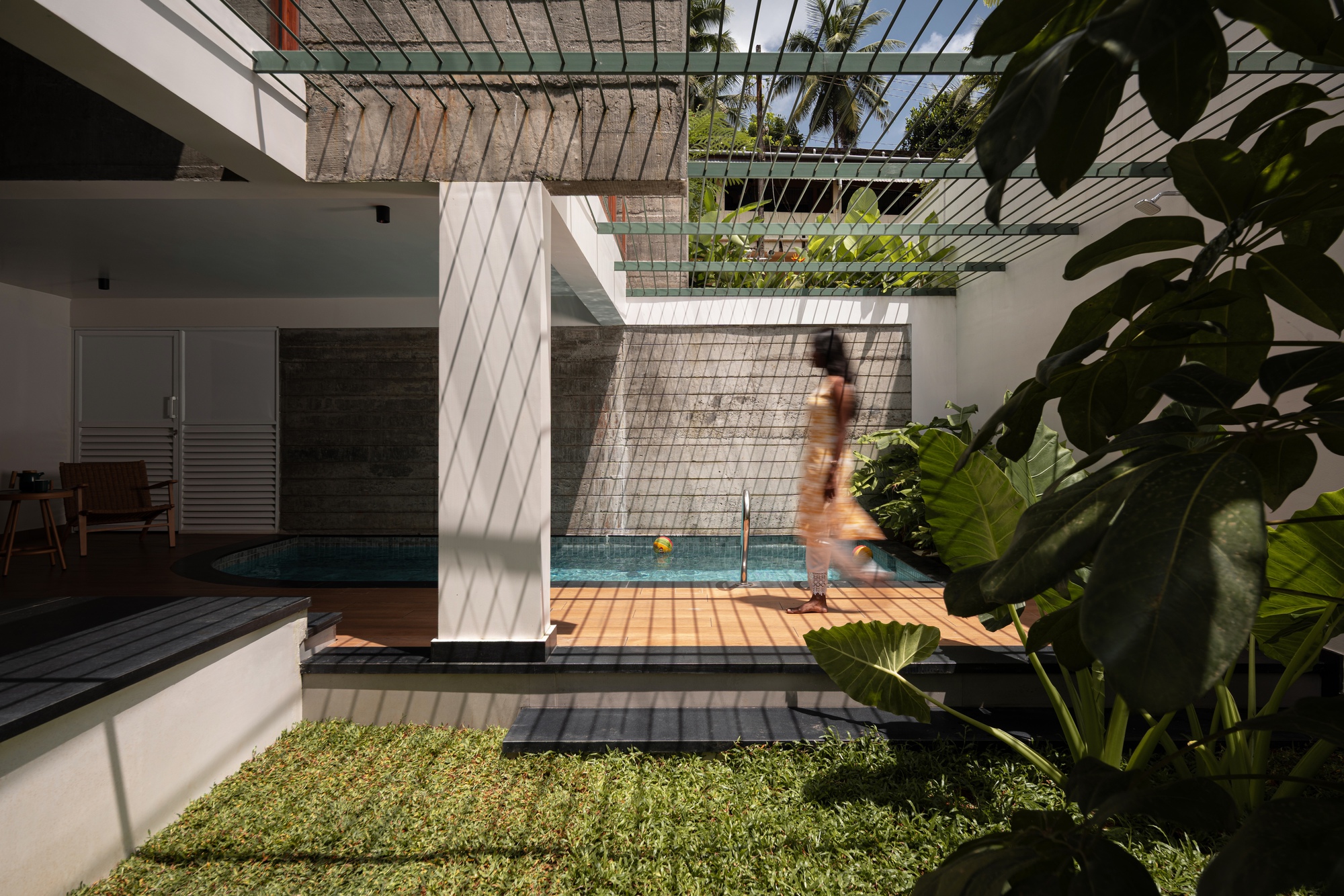 Courtyard pool with timber deck and overhead trellis casting diagonal shadows on white walls