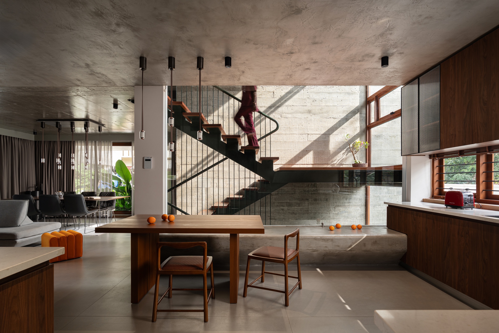 Open living and dining space with steel staircase beneath board-formed concrete ceiling and walls