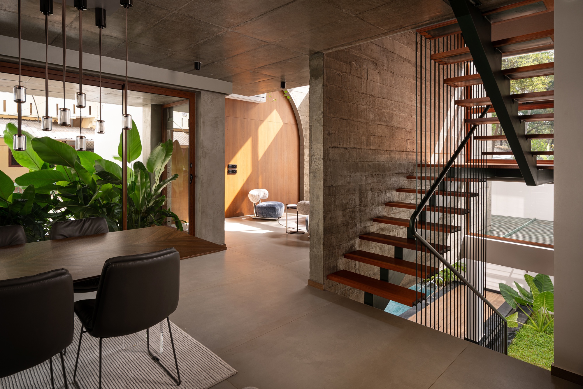 Open-tread timber staircase with vertical metal railings descending past concrete walls and pendant light clusters