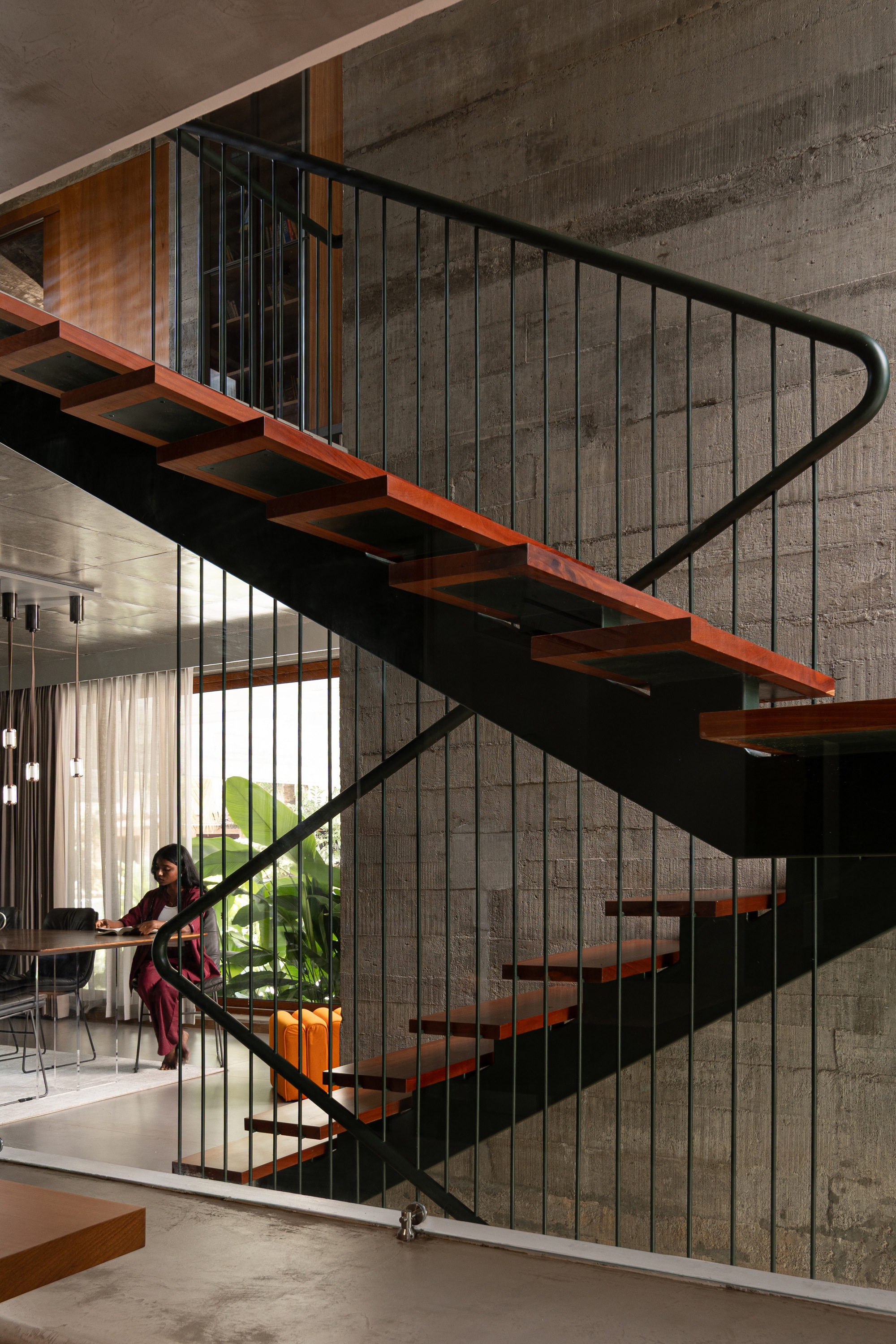 Timber and steel staircase with vertical rod balustrade against board-formed concrete wall as a person ascends