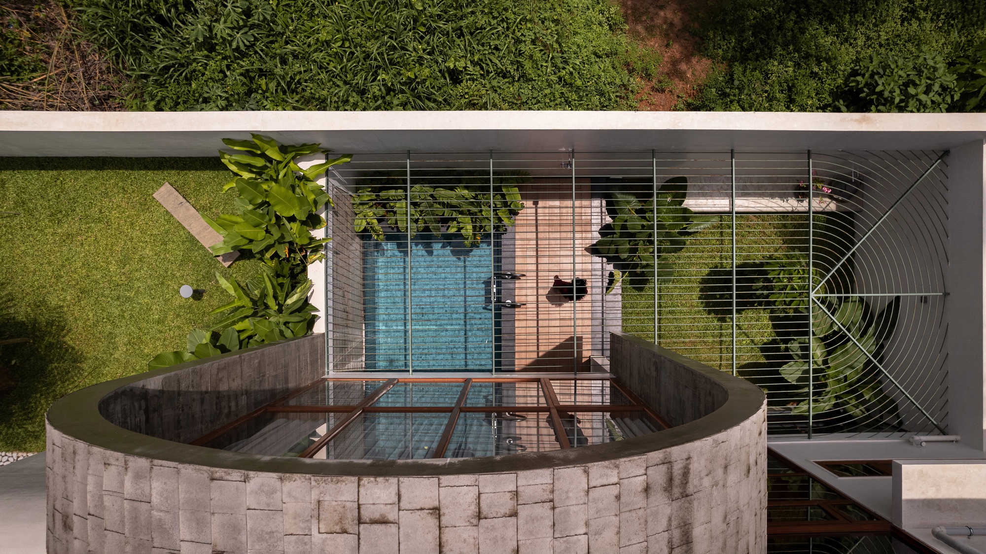 Aerial view of the curved concrete water feature with tile surround and reflecting pool below glass-walled living space