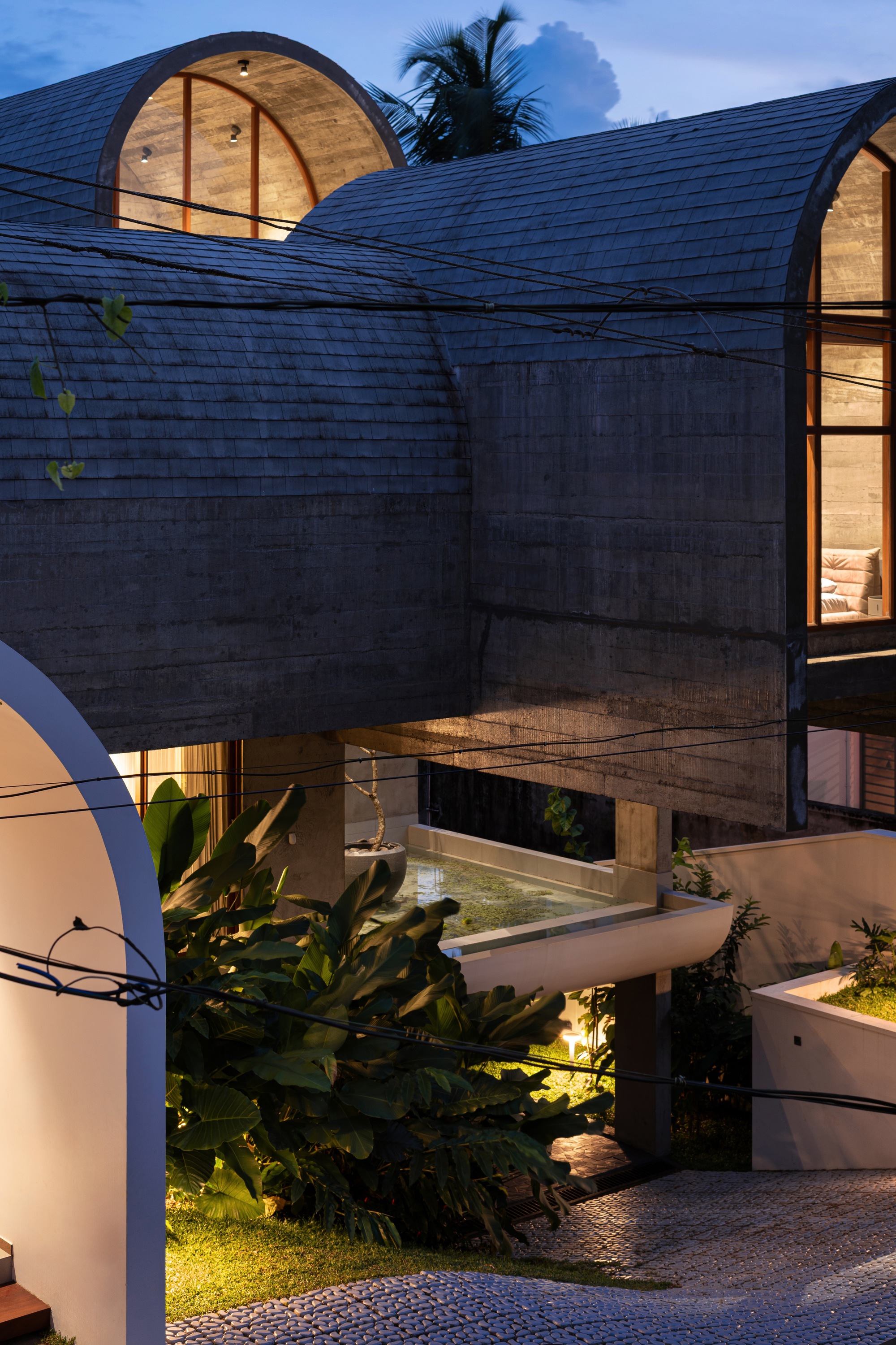 Courtyard view of the barrel-vaulted roofs with illuminated arched windows and tropical plantings at dusk