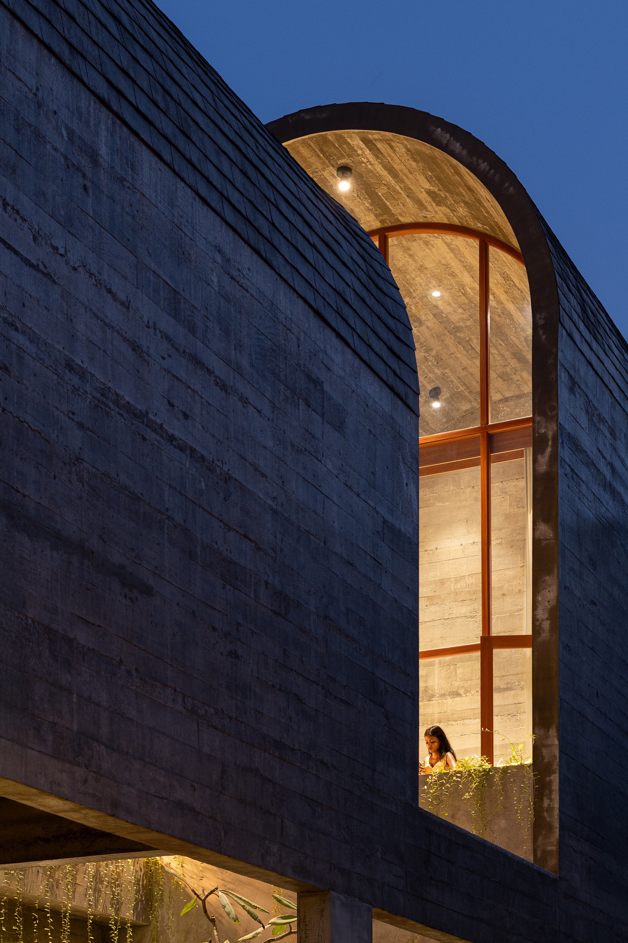 Arched window alcove with timber ceiling and vertical glazing bars framing a figure at twilight