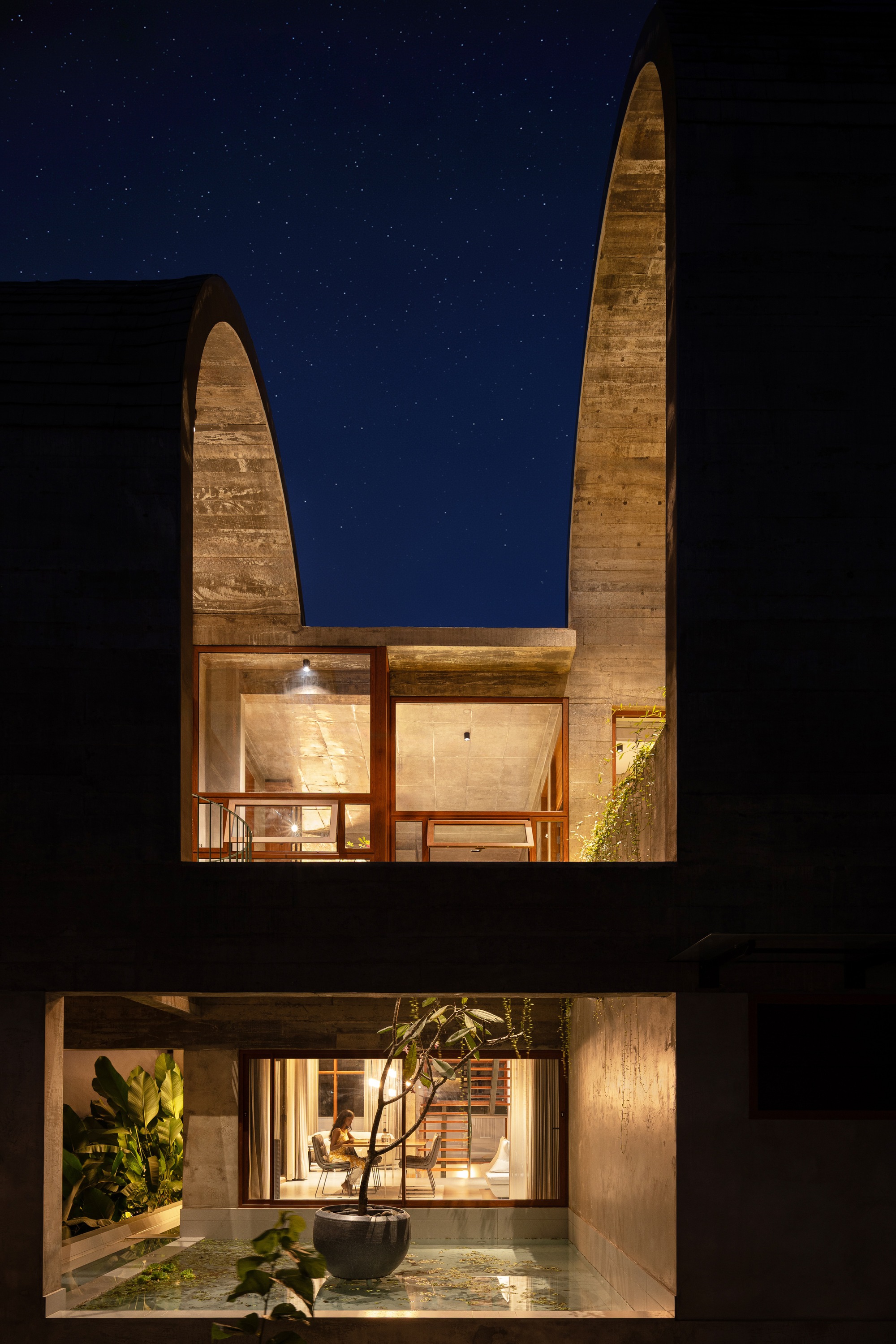 Night view of the concrete barrel vault and entry courtyard with potted tree under a starry sky