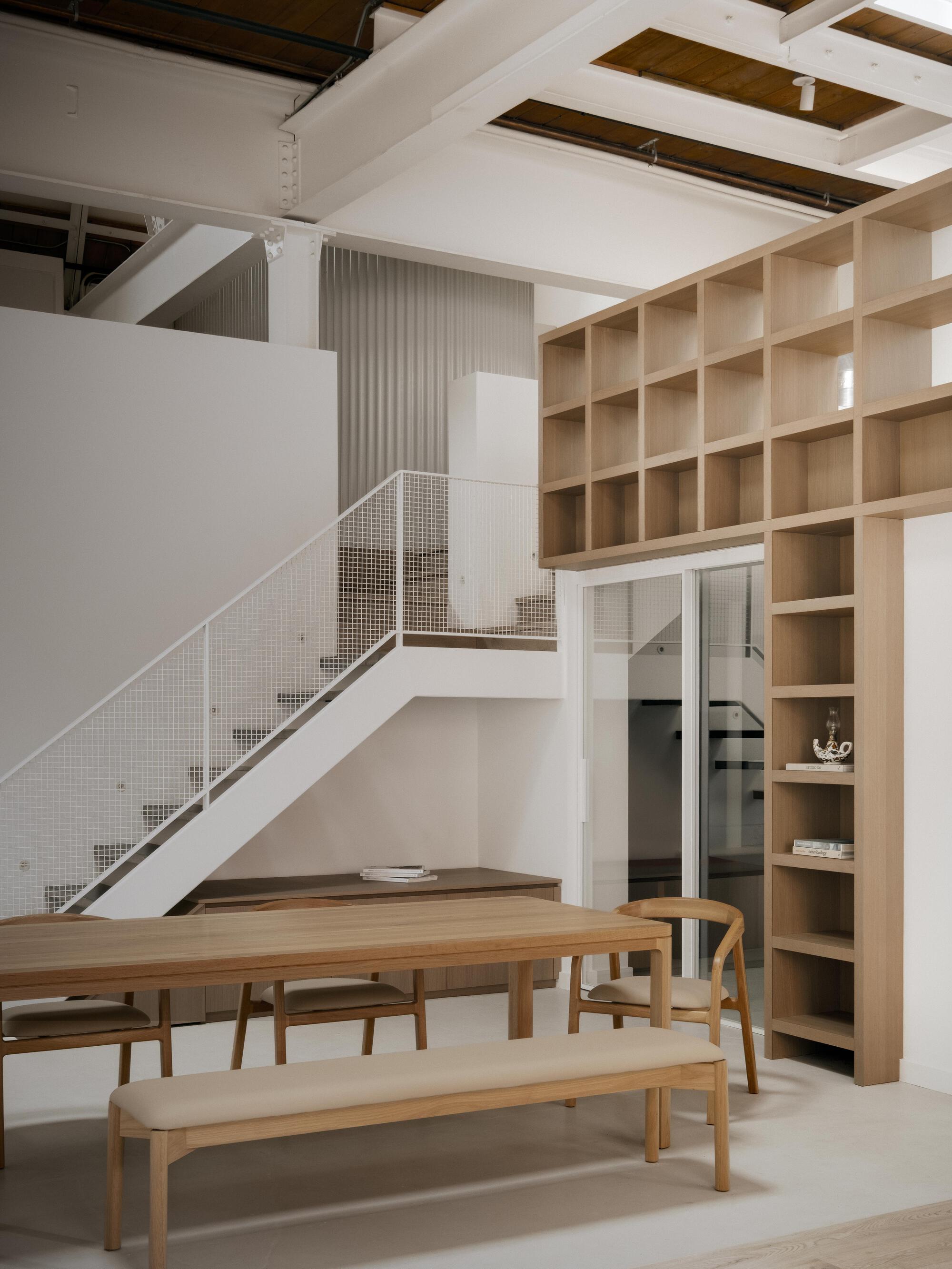 View of the white staircase with perforated metal balustrade beneath a floor-to-ceiling timber shelving wall
