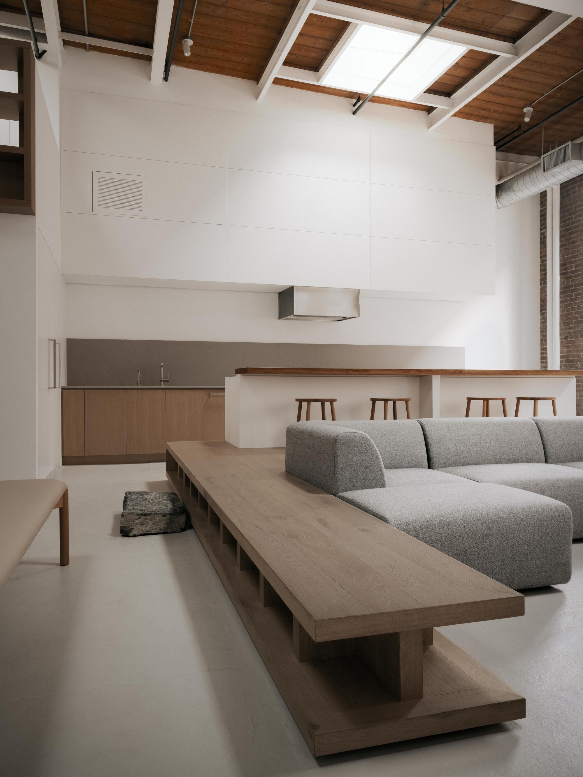 Open-plan living space with timber kitchen counter and grey sectional sofa under exposed wood-beam ceiling