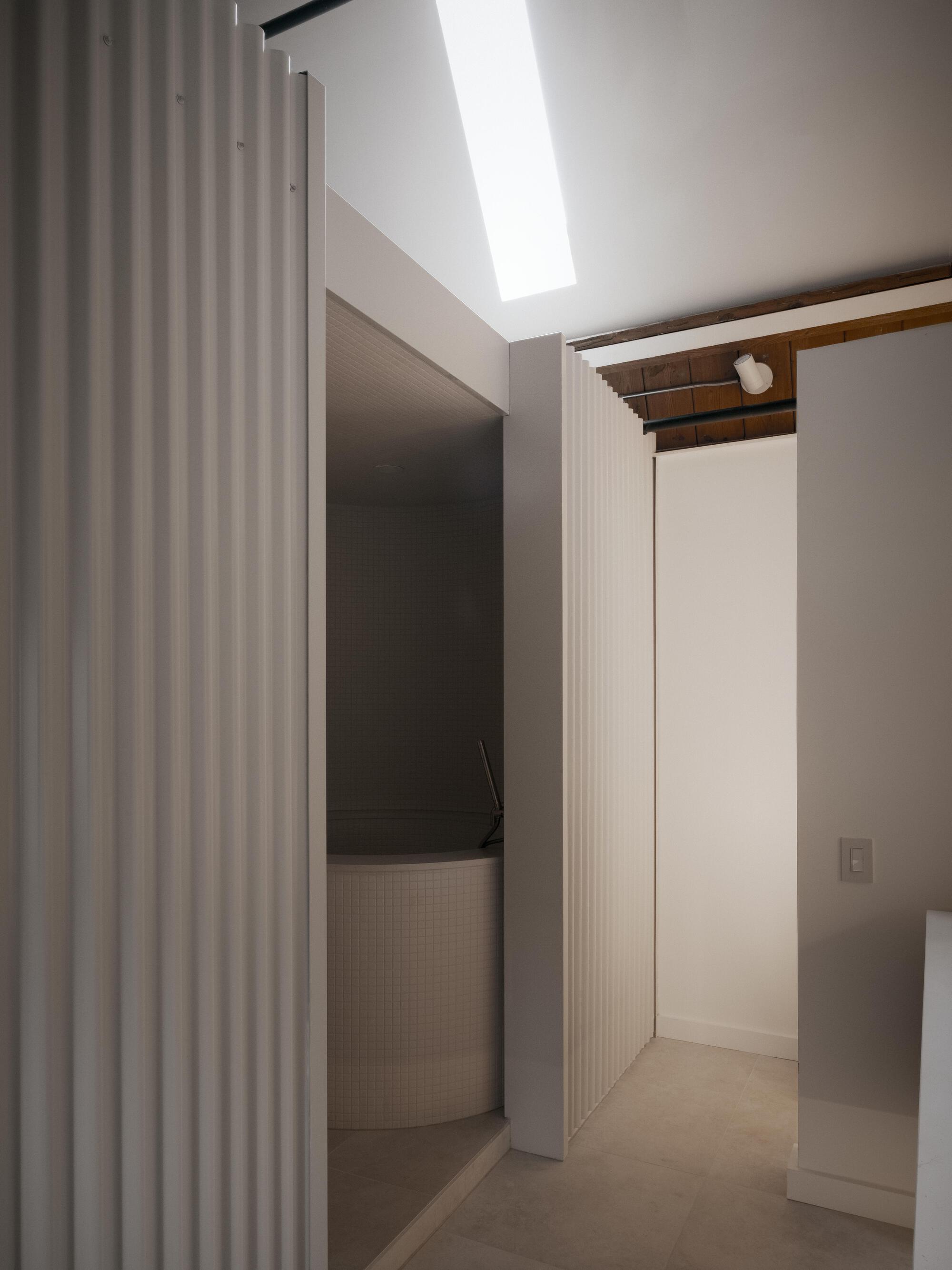 Interior hallway with fluted wall panels and a linear skylight casting daylight onto white surfaces