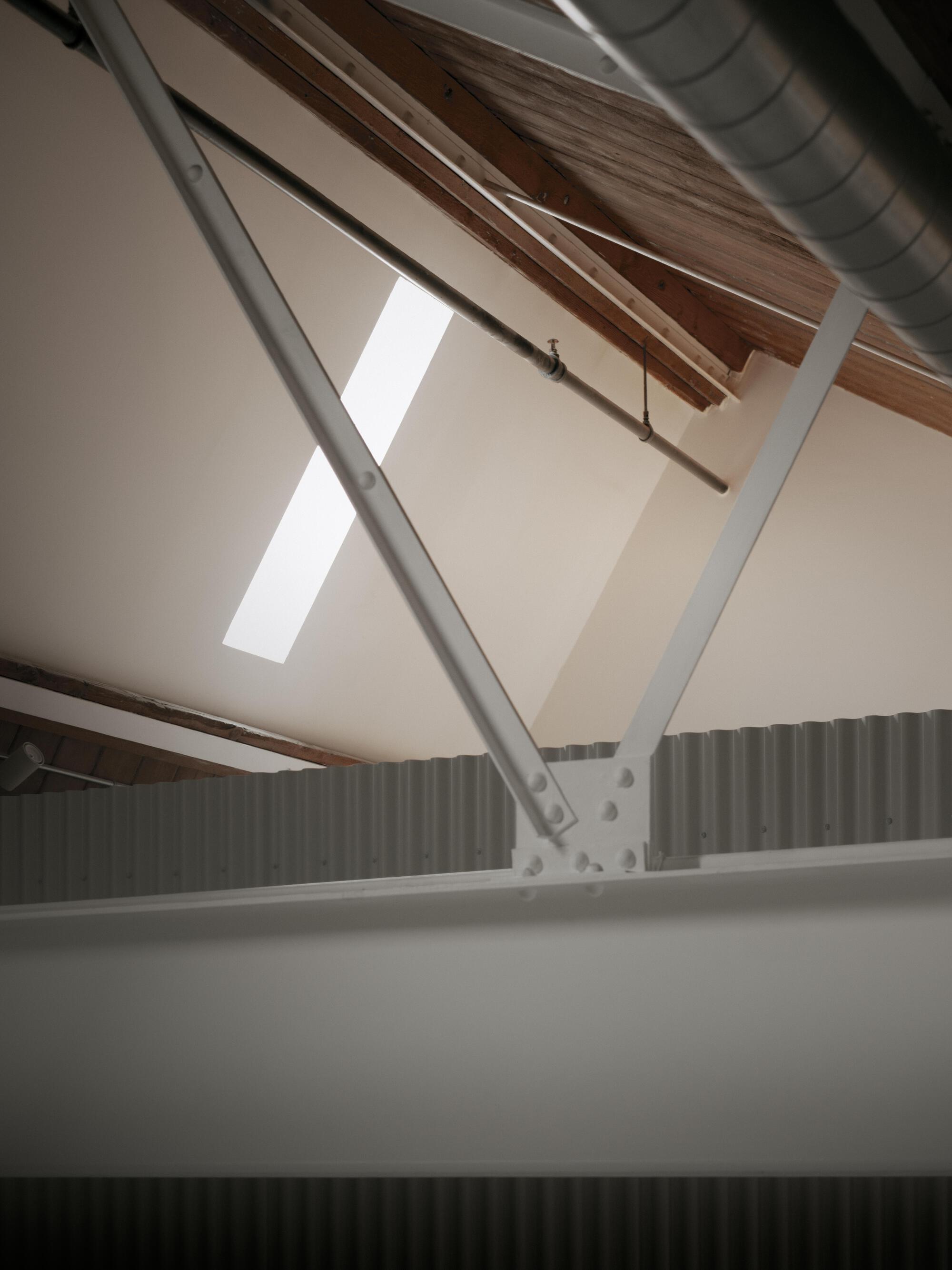 Upward view of exposed timber beams and steel ventilation ductwork beneath a skylight