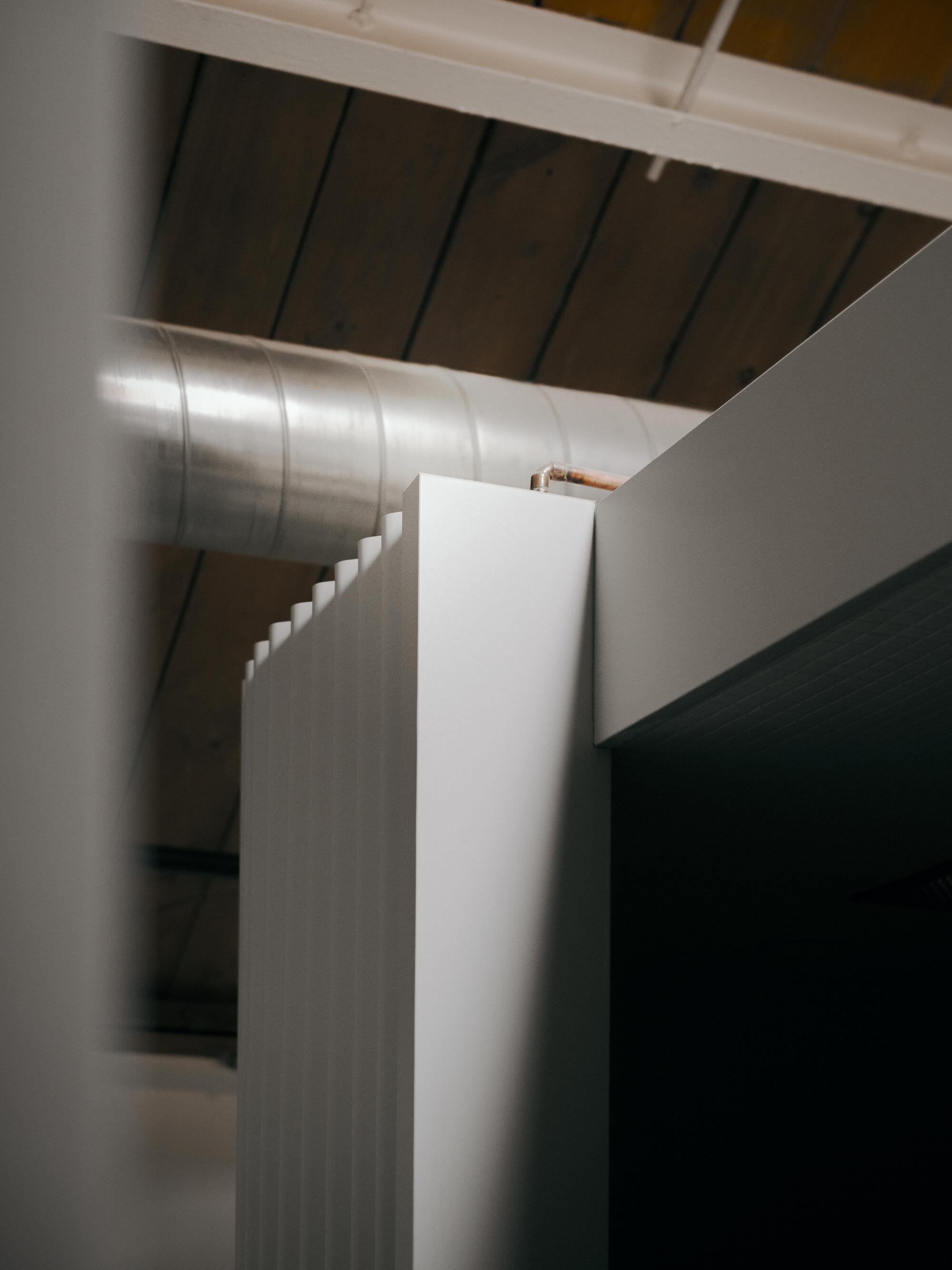 Angled interior corner showing fluted wall panel beside exposed ducting and timber ceiling planks