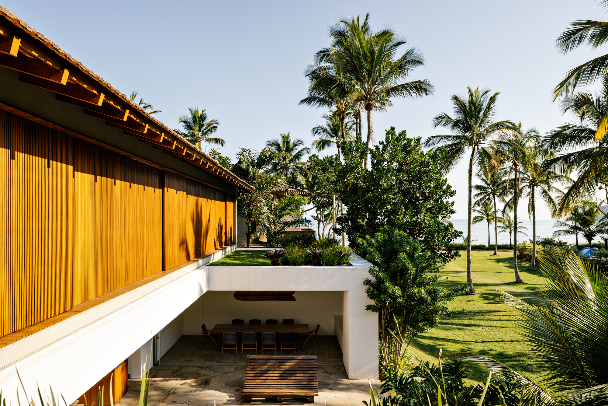 Upper terrace with vertical timber cladding overlooking a sunken outdoor dining area surrounded by palms