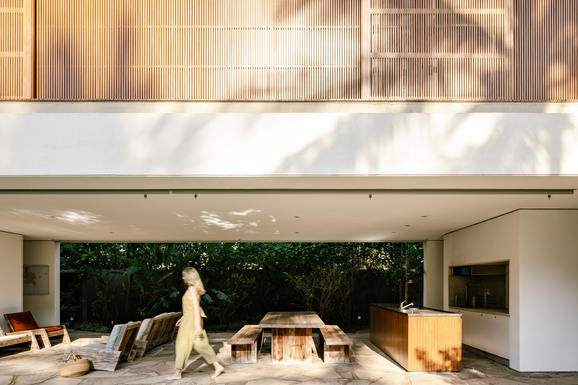 Covered terrace with timber dining table and figure walking past vertical timber cladding above