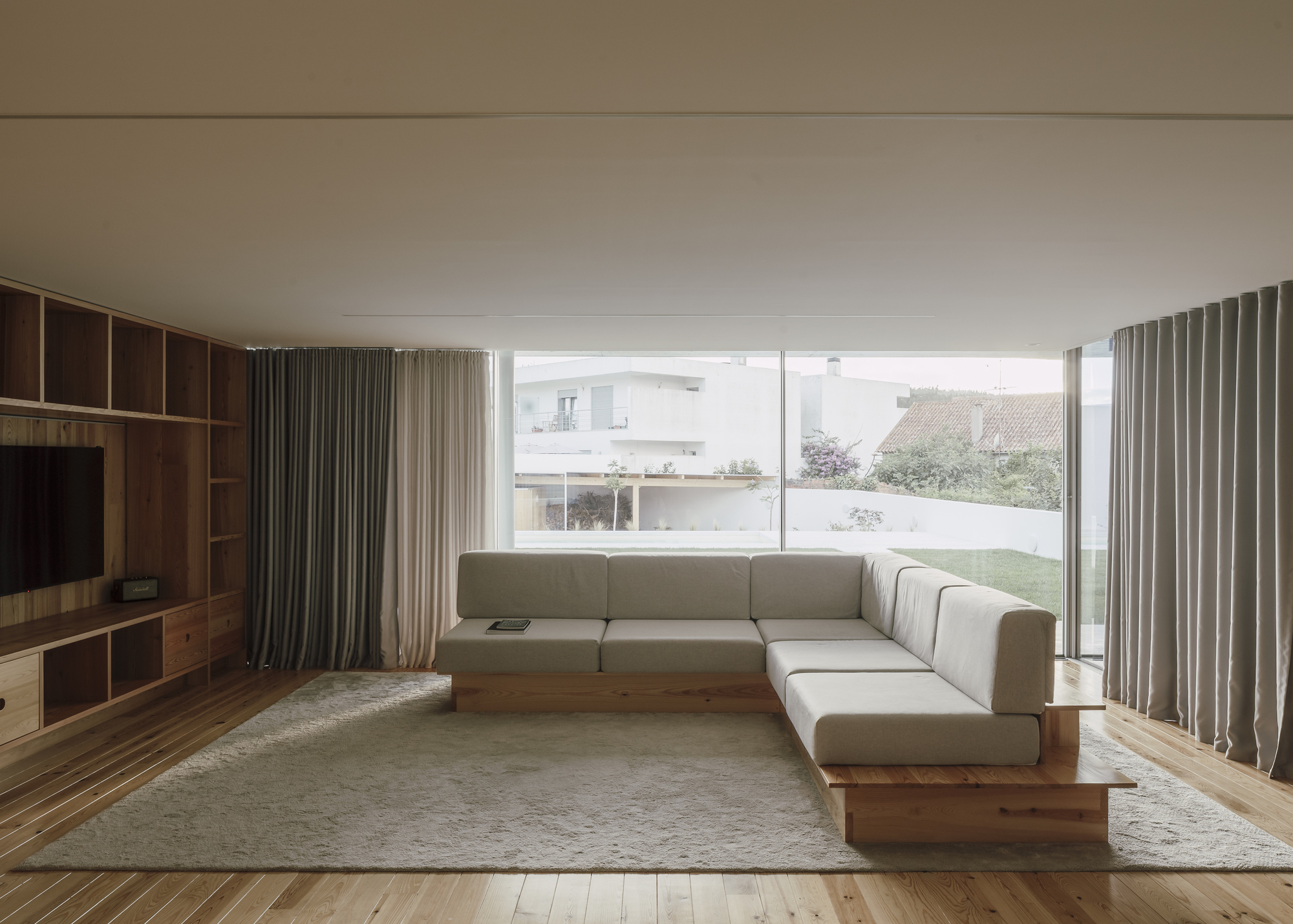 Living room with corner sofa facing full-height glazing overlooking lawn and neighboring rooftops