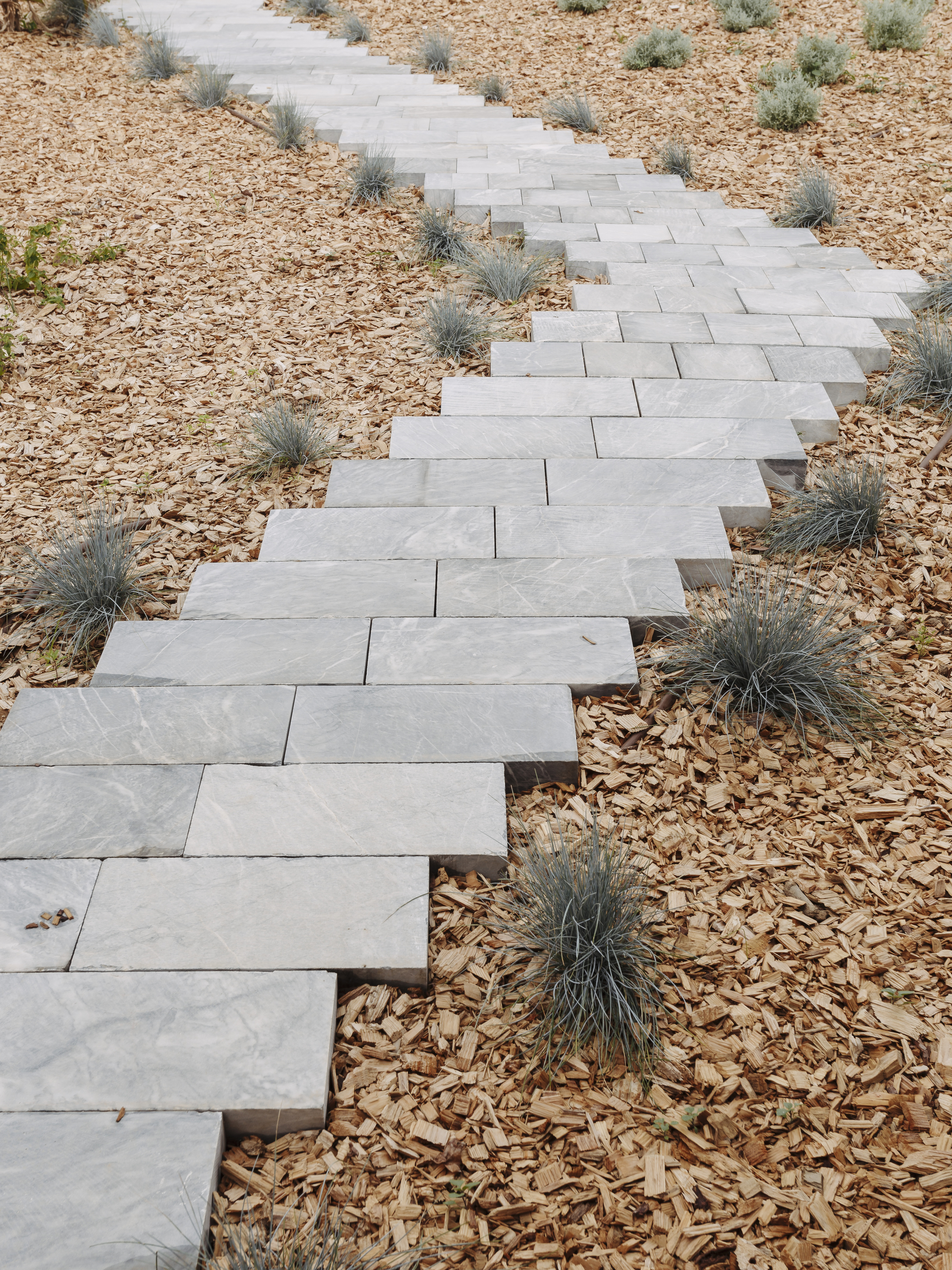 Stone paver pathway zigzagging through gravel mulch and low grasses in a dry landscape
