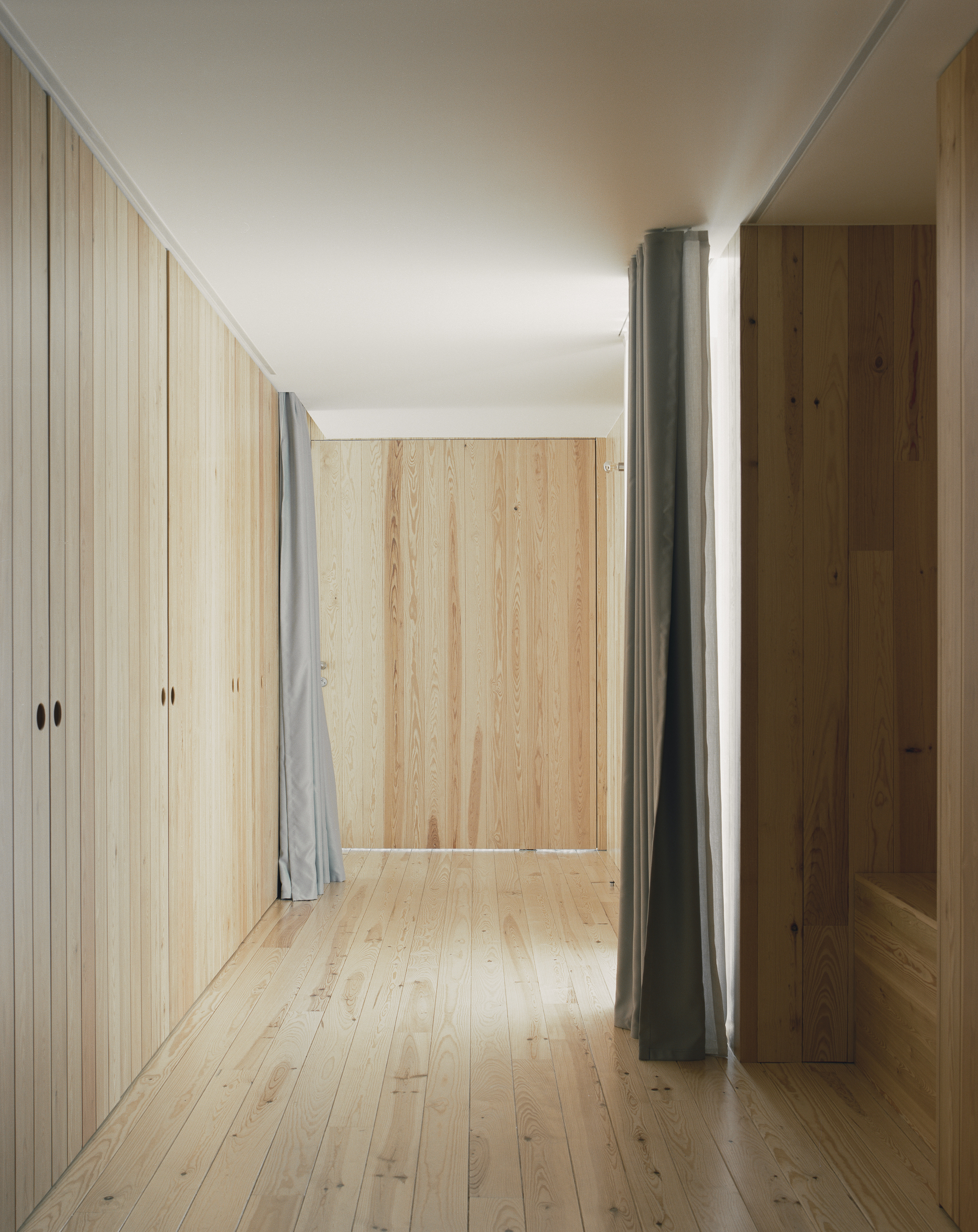 Interior hallway with vertical timber paneling and a grey fabric curtain beside a steel column
