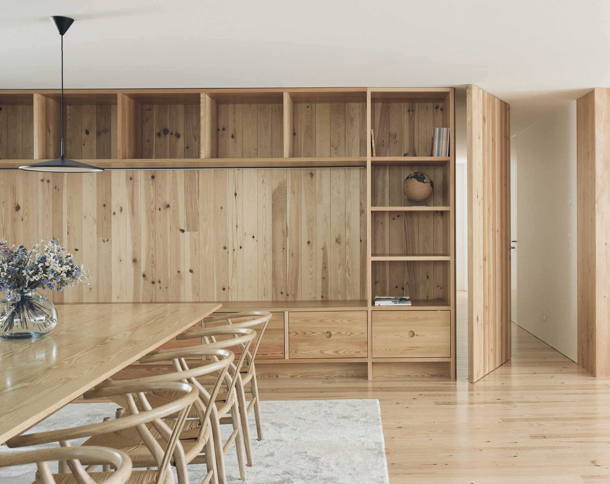 Dining area with timber storage wall, open shelving, and chairs around a long table