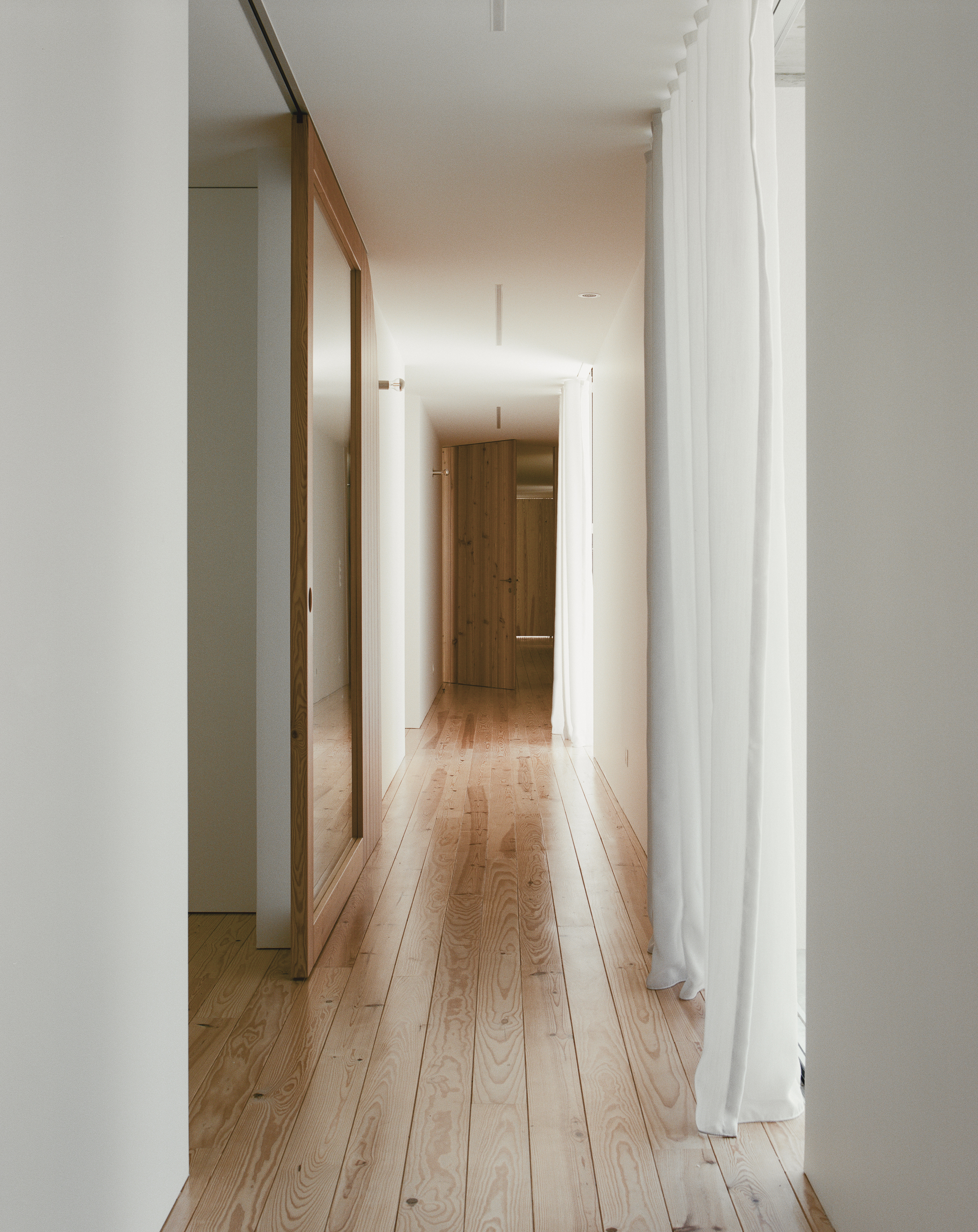 White hallway with timber sliding door and oak flooring lit by recessed ceiling fixtures