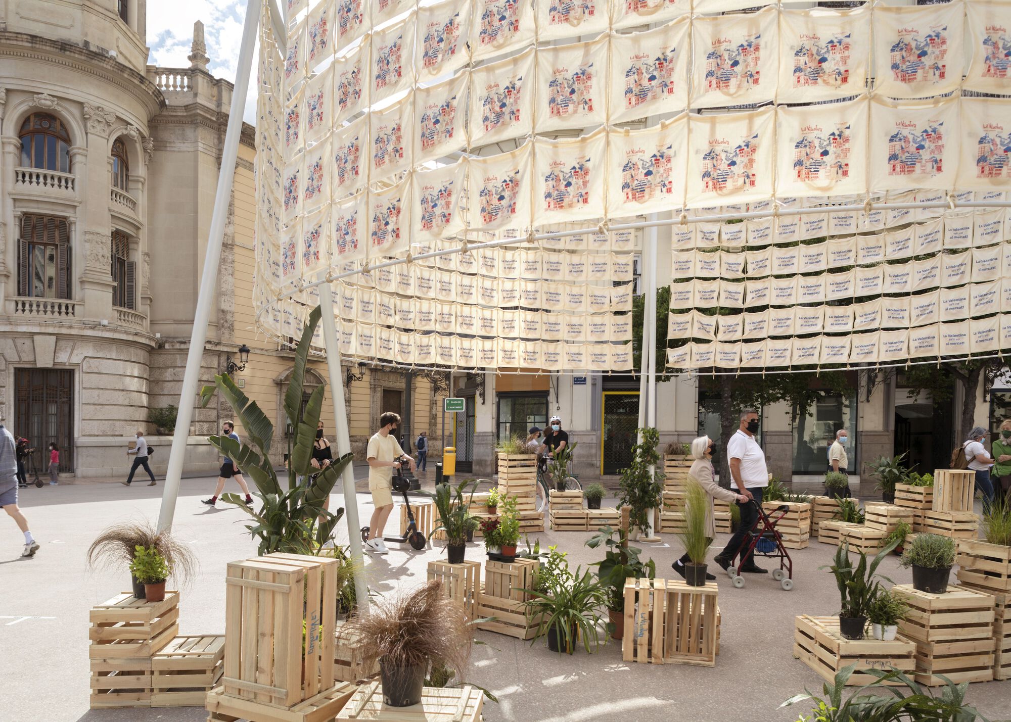 Close view of the printed textile facade with stacked wood benches and greenery below the canopy