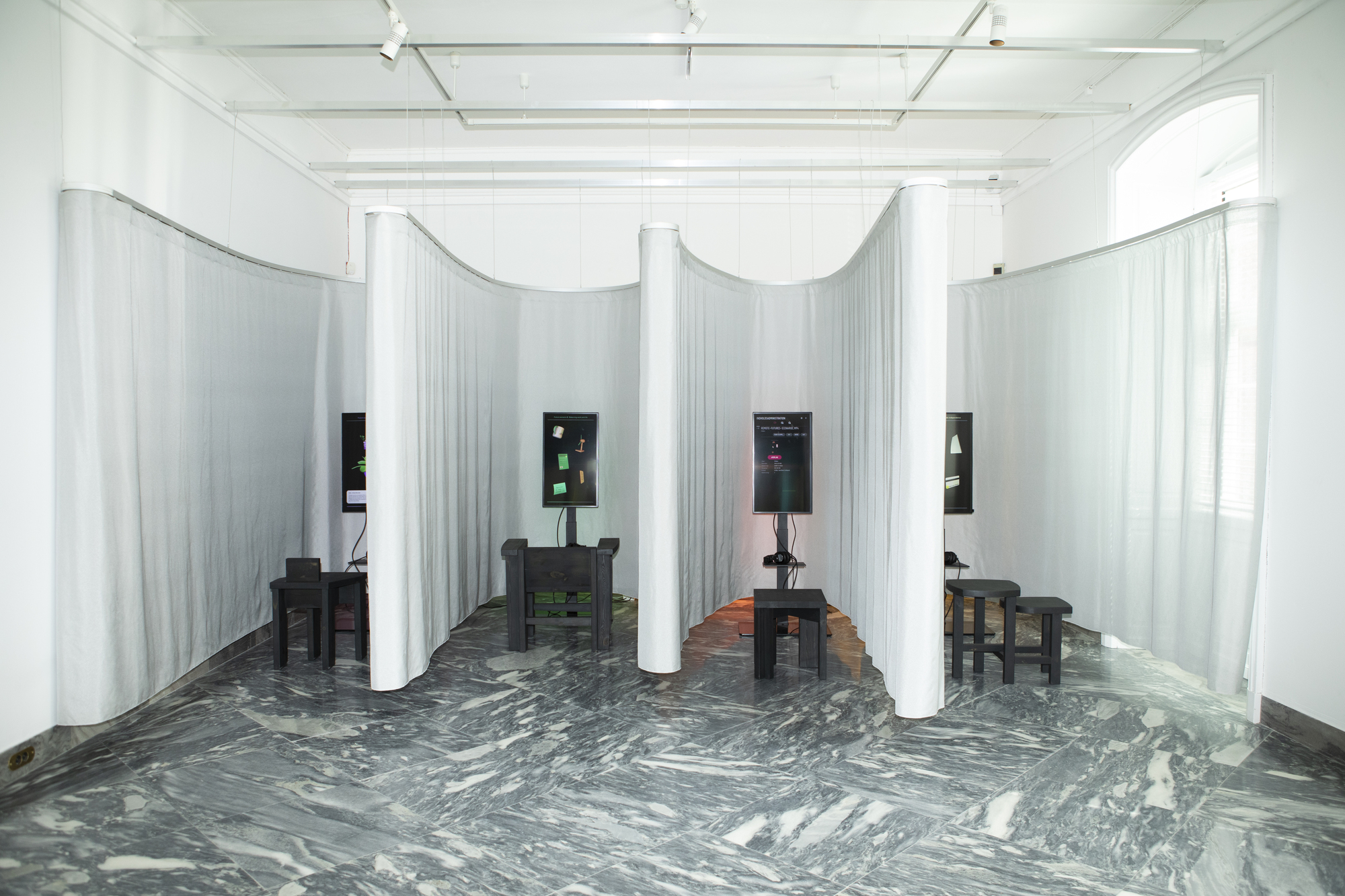 Exhibition space with curved white curtain partitions and swirling grey marble floor under track lighting