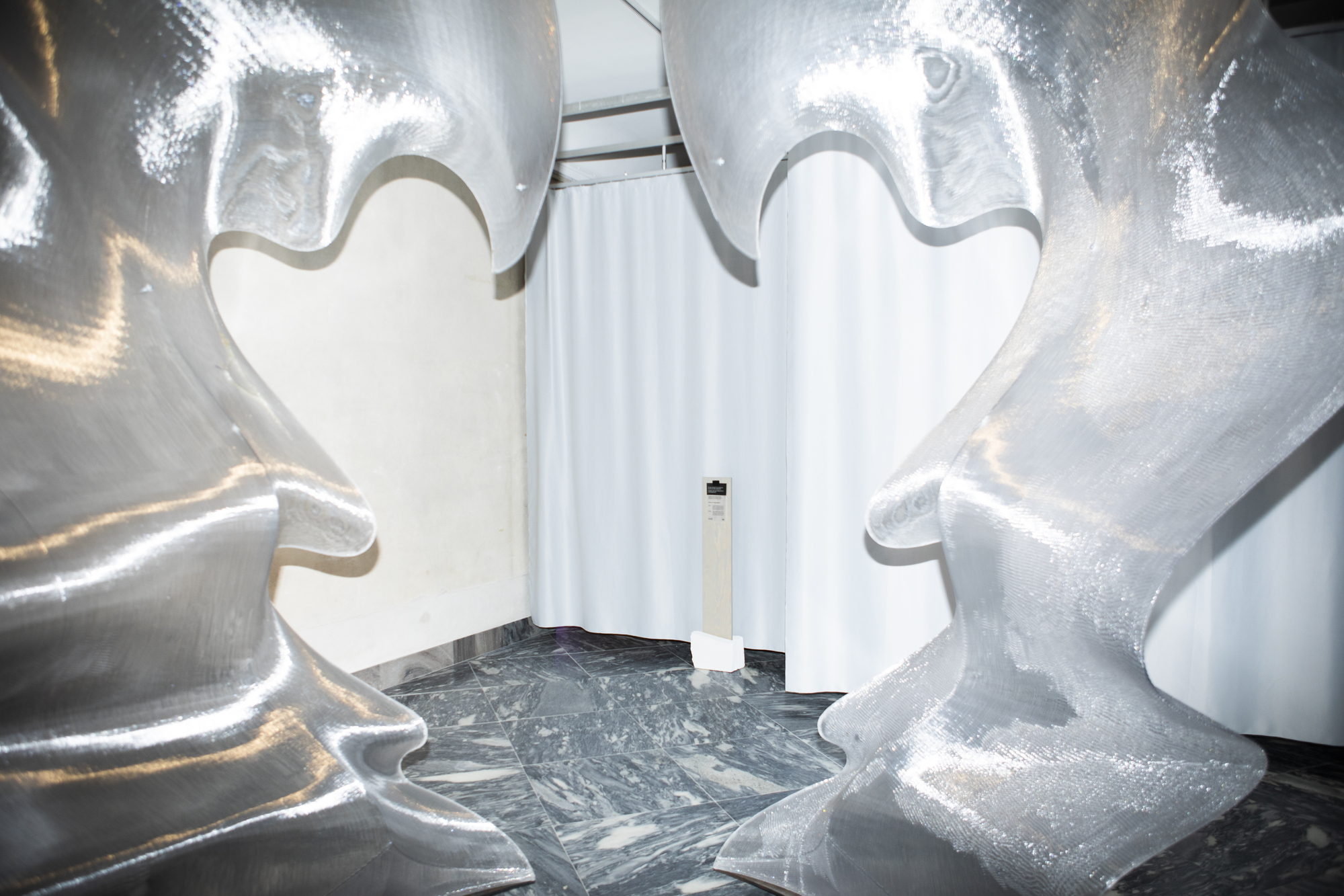 Close-up of inflated metallic sculptural forms arranged in corner space with white curtain backdrop