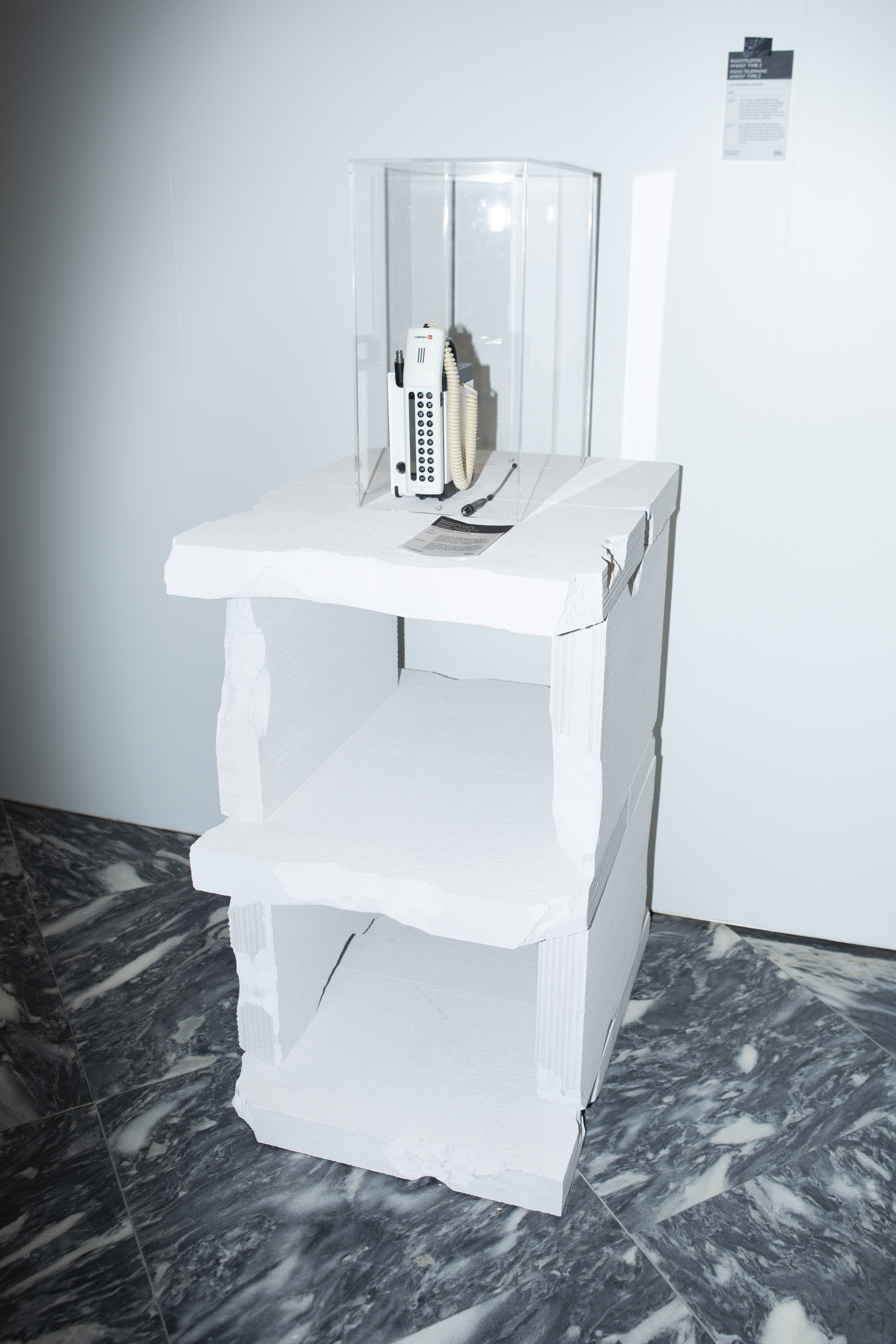 White tiered display stand with architectural models and remote control on dark marbled floor