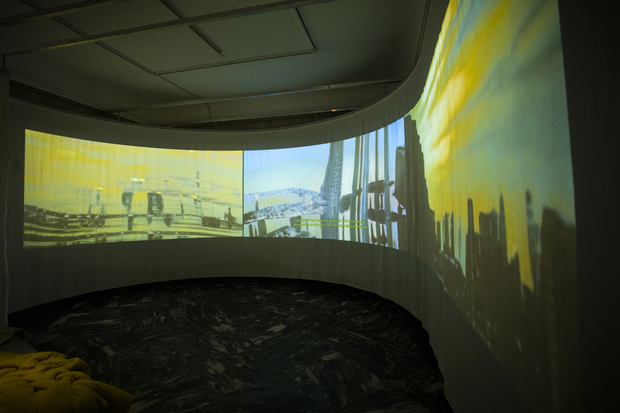 Curved projection screen displaying urban imagery in darkened room with marble floor