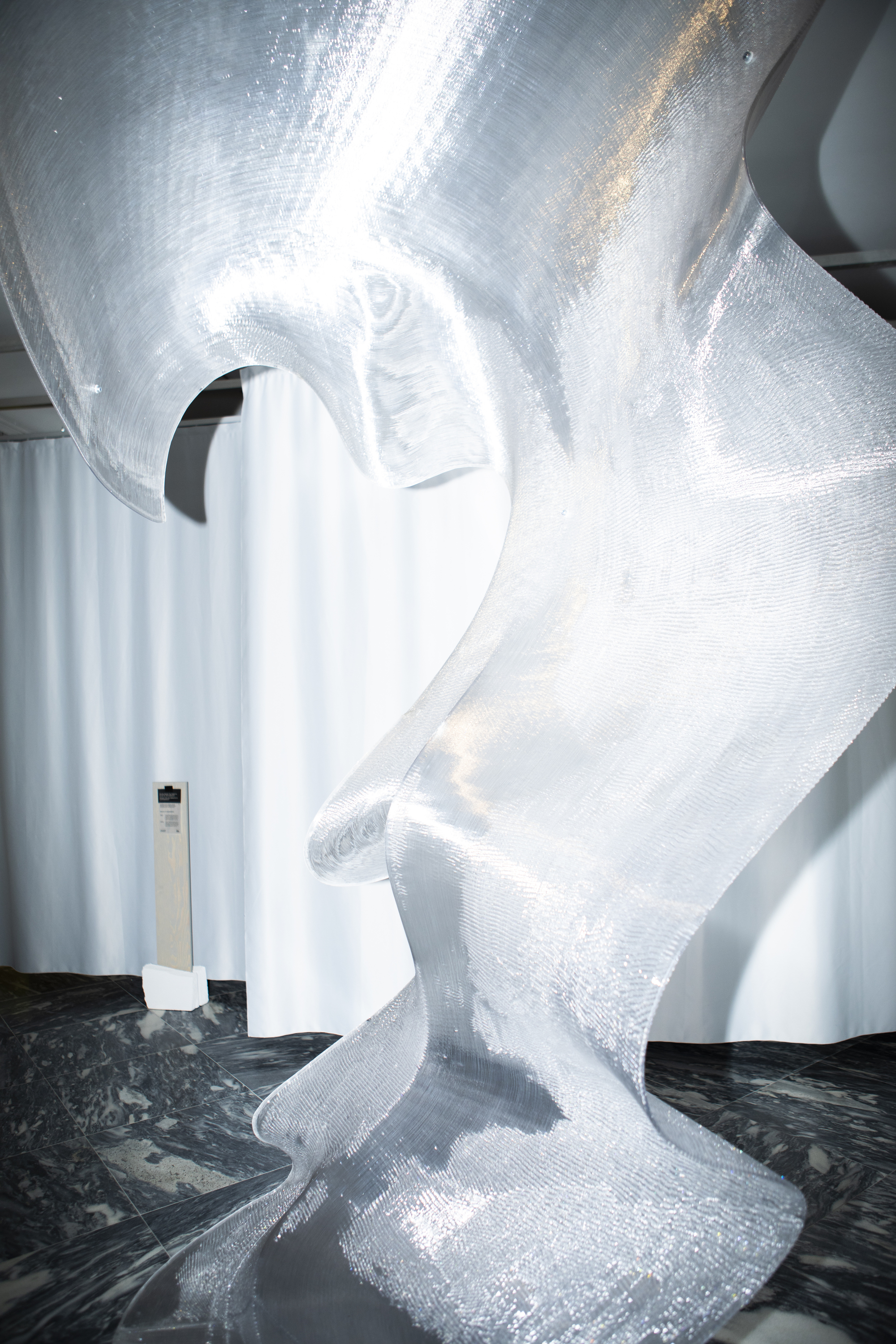 Translucent white sculptural column with spiral ridges rising from black marbled floor