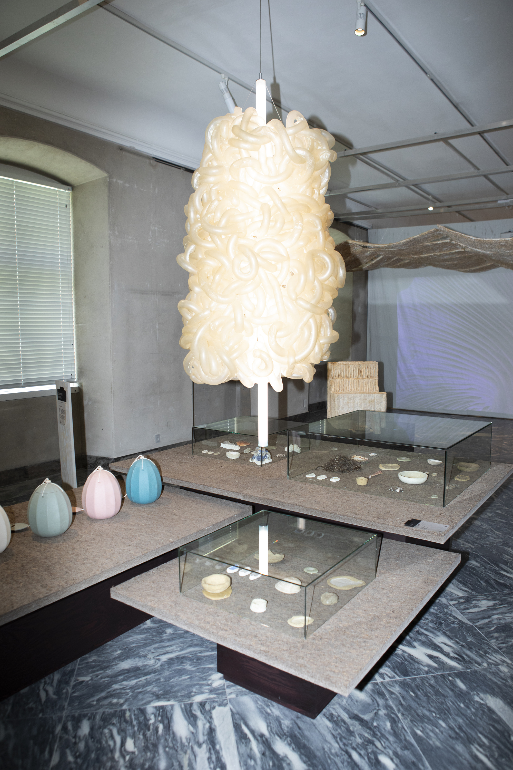 Exhibition space with suspended cream pendant light above terrazzo display tables and glass vitrines