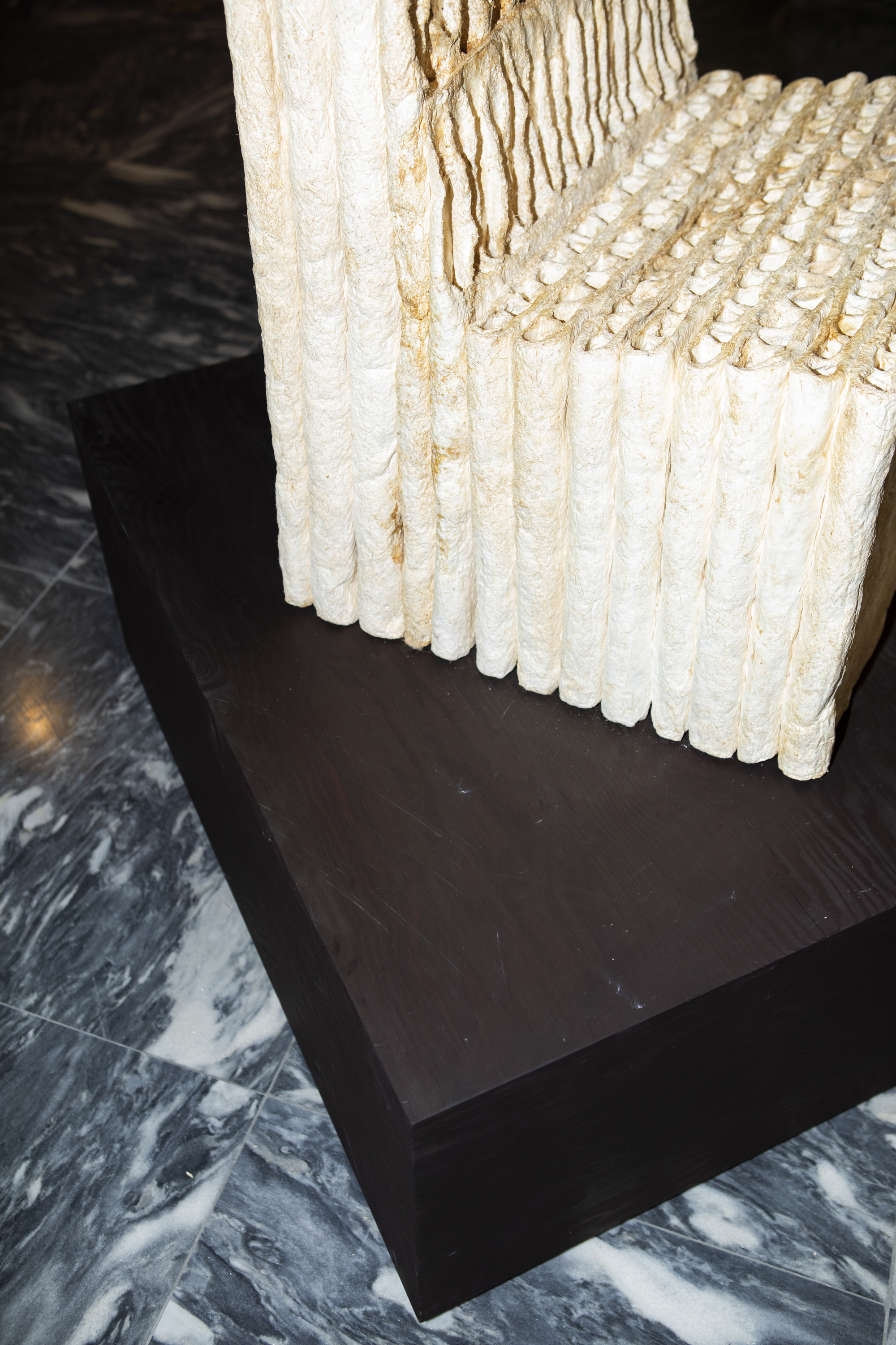 Detail of white cylindrical material sample resting on dark plinth above marbled floor