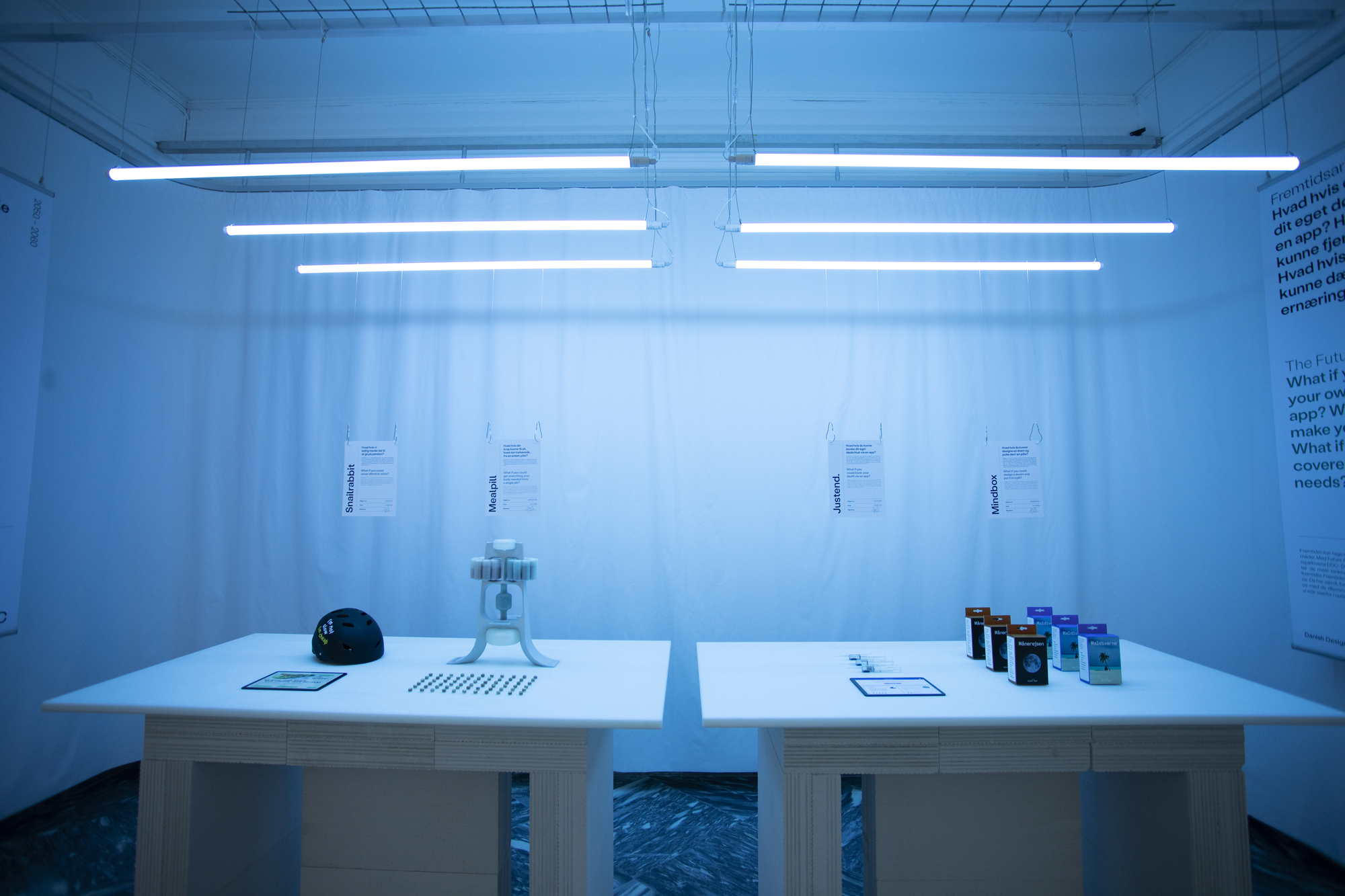 White display table with material samples beneath fluorescent tube lighting and sheer curtain backdrop