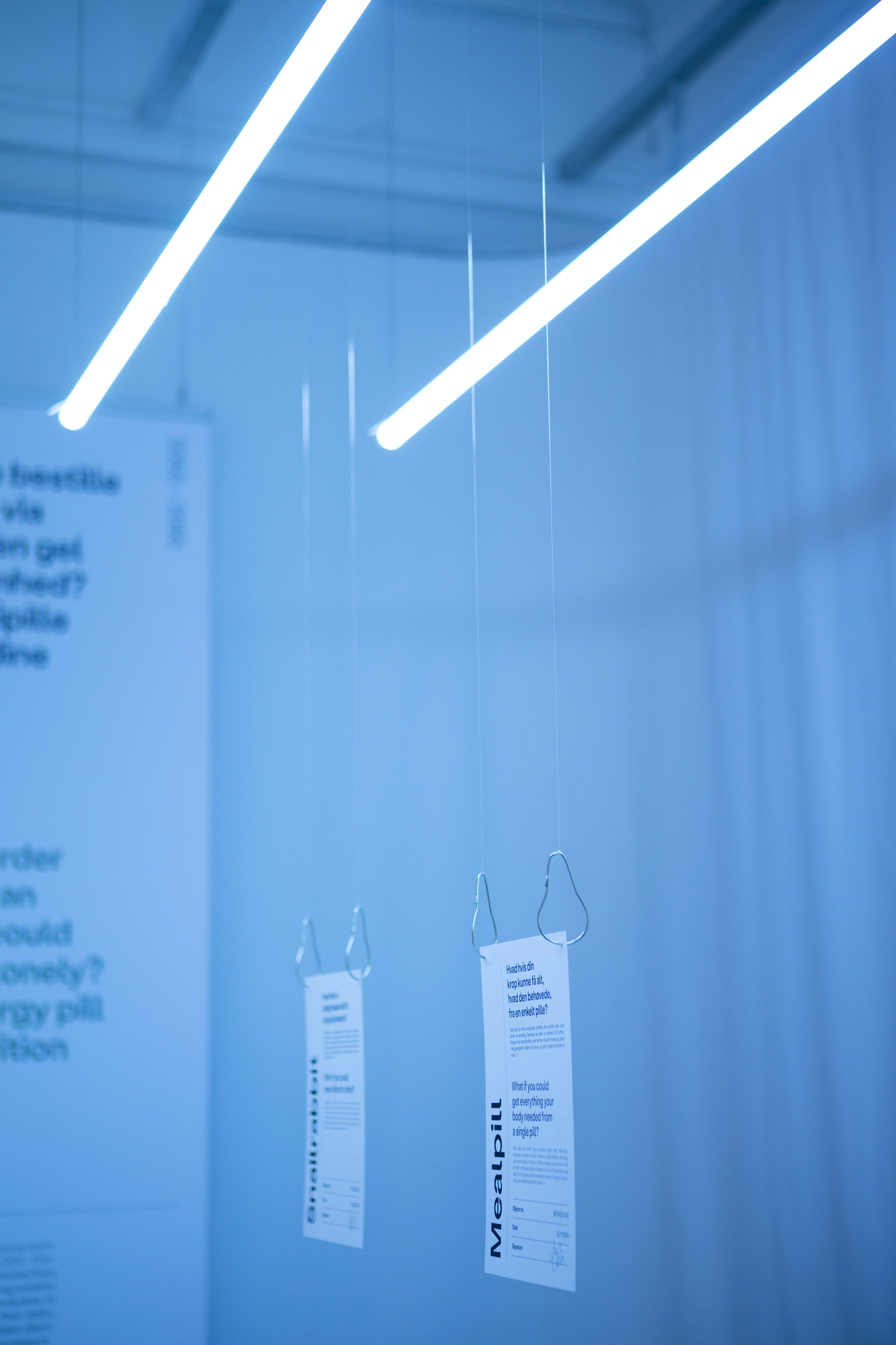 Linear pendant light fixtures suspended above translucent curtains with text and hanging information tags
