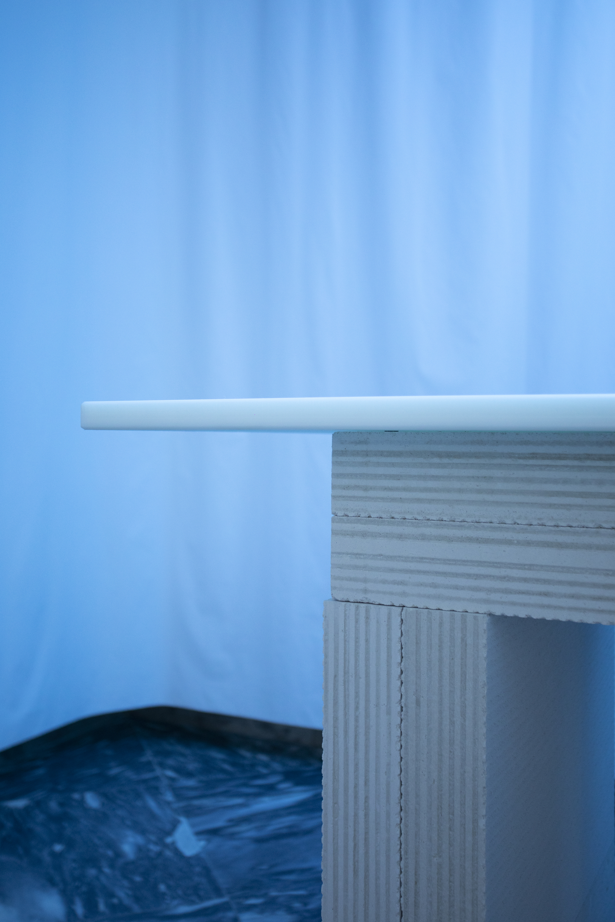 Close-up of corrugated cardboard table edge with white rounded top against a blue curtain