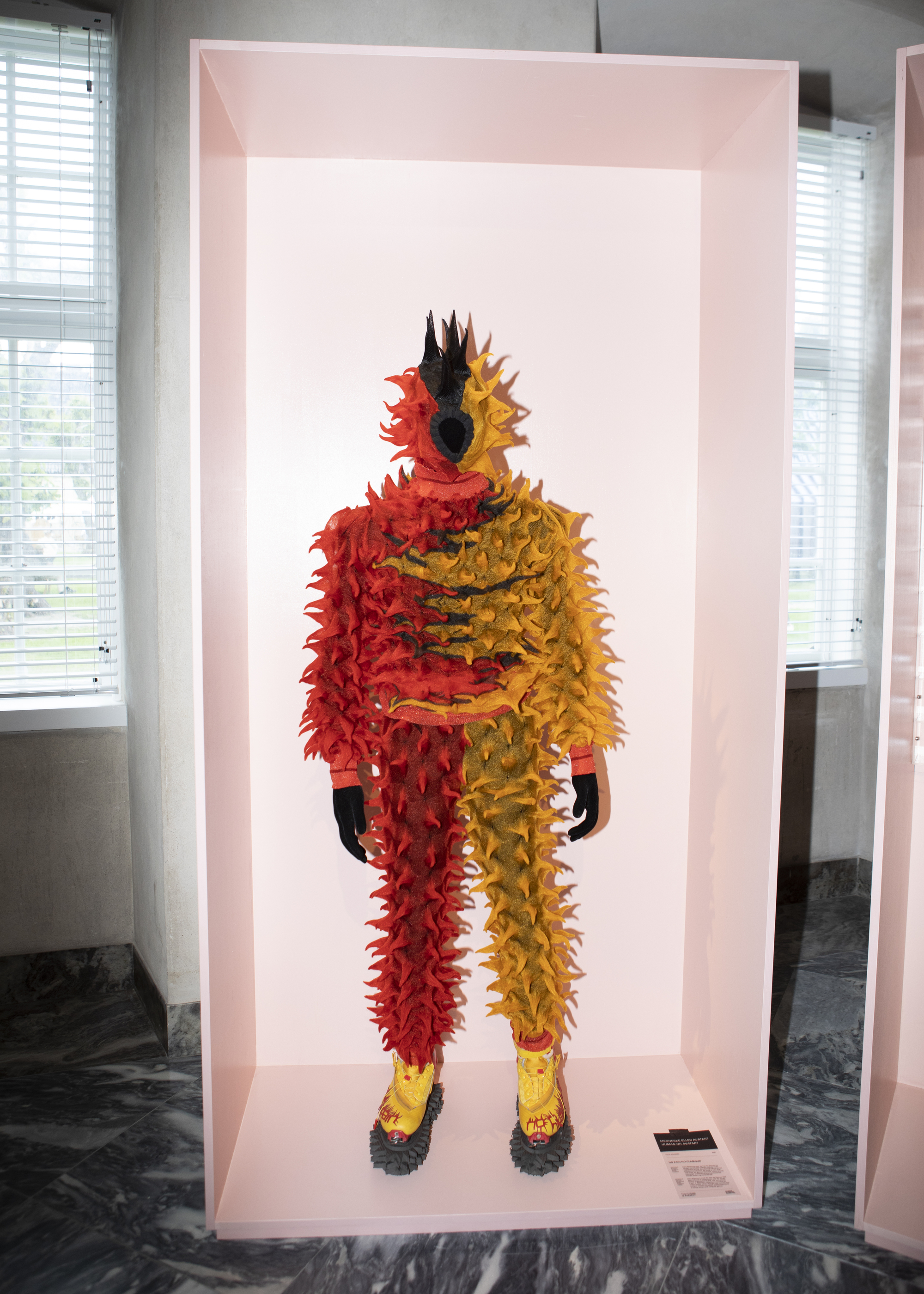 Feathered costume in red and yellow displayed within a pink-lit exhibition alcove