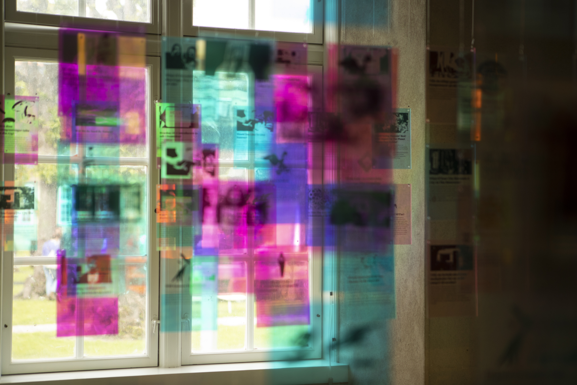 Layered translucent colored panels mounted on windows creating overlapping magenta and cyan reflections