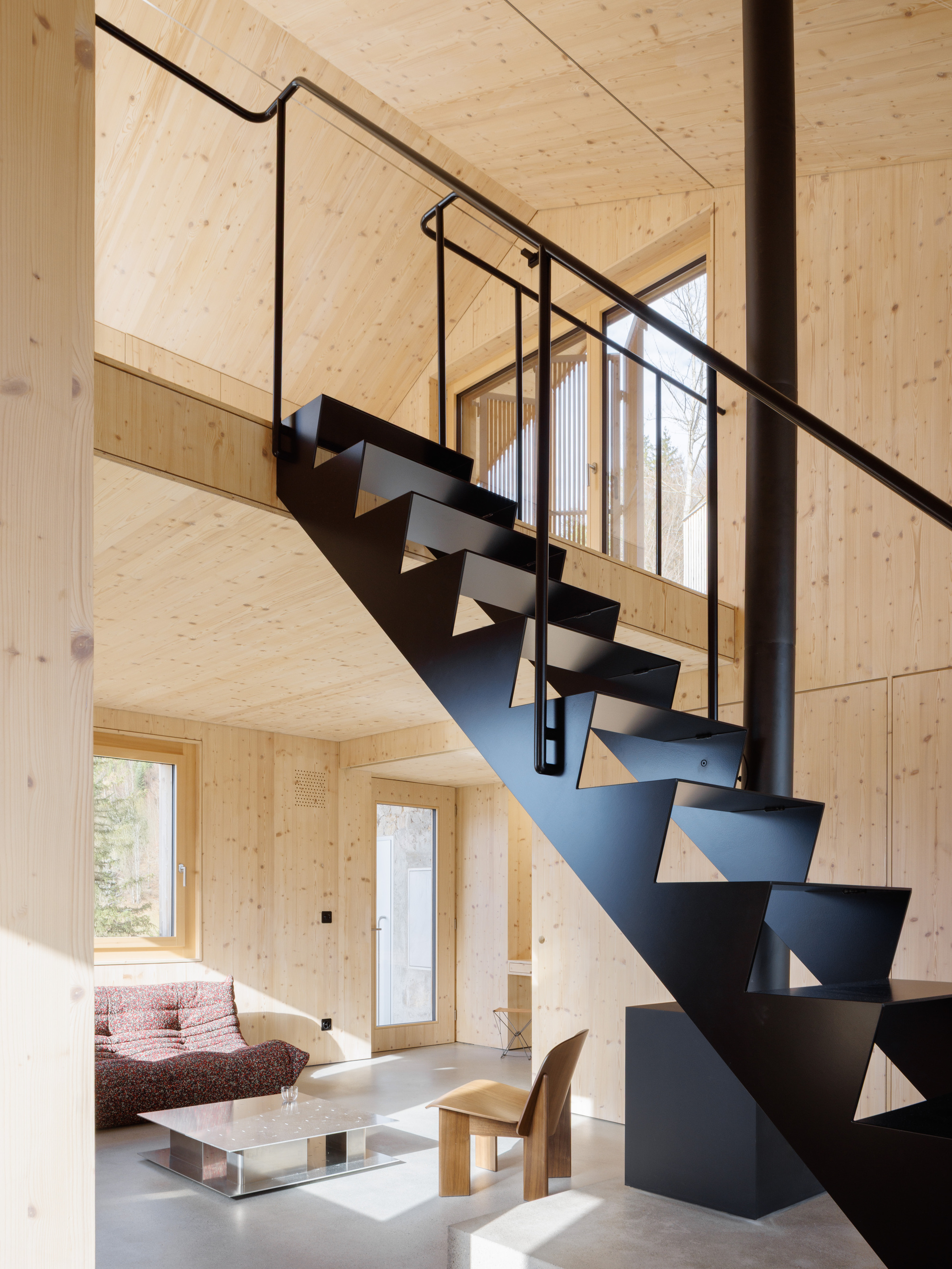 Folded steel staircase with triangular cutout treads and tubular handrail against pale plywood walls