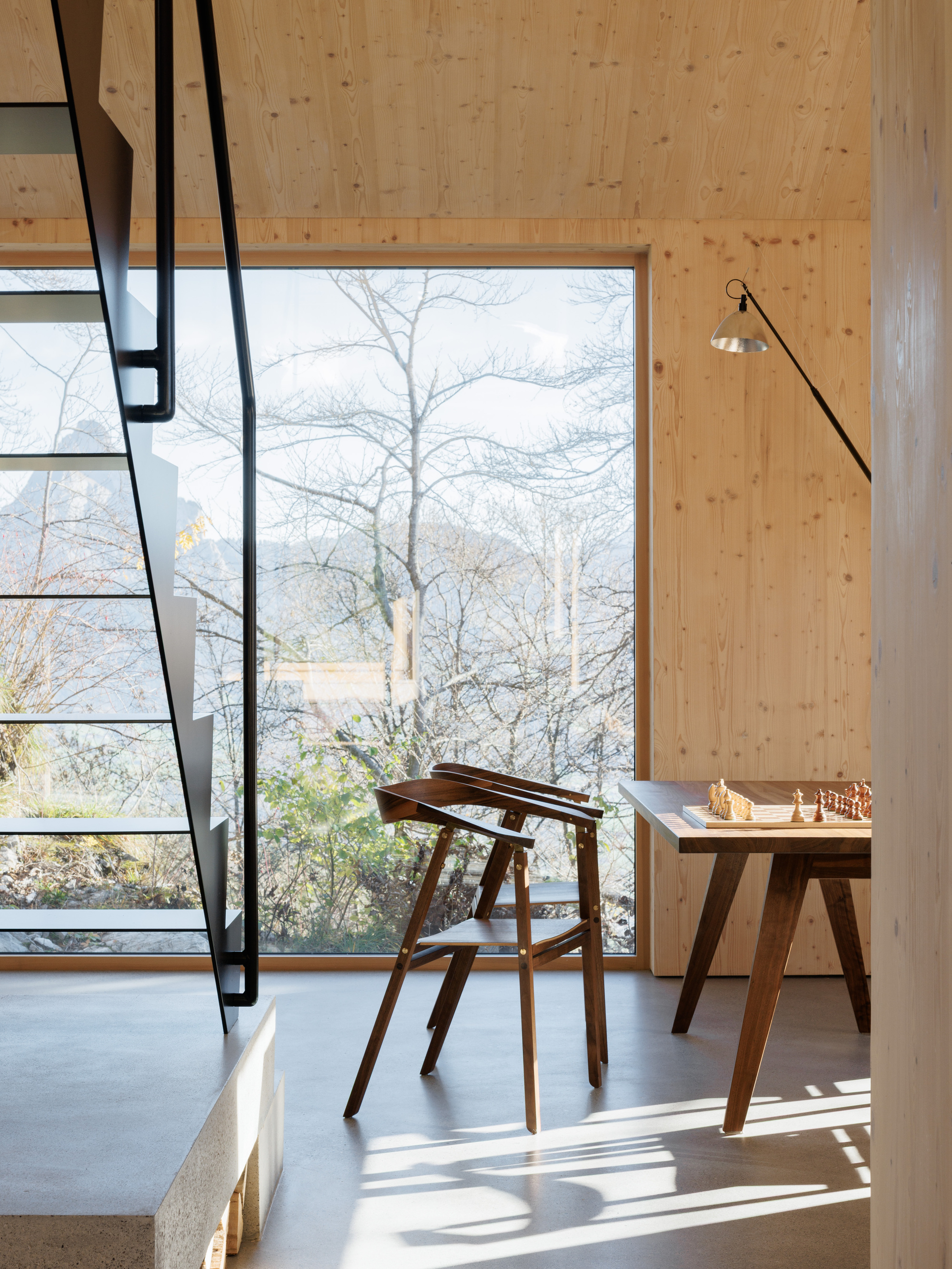 Interior with black steel staircase, timber wall paneling, full-height window framing bare winter trees